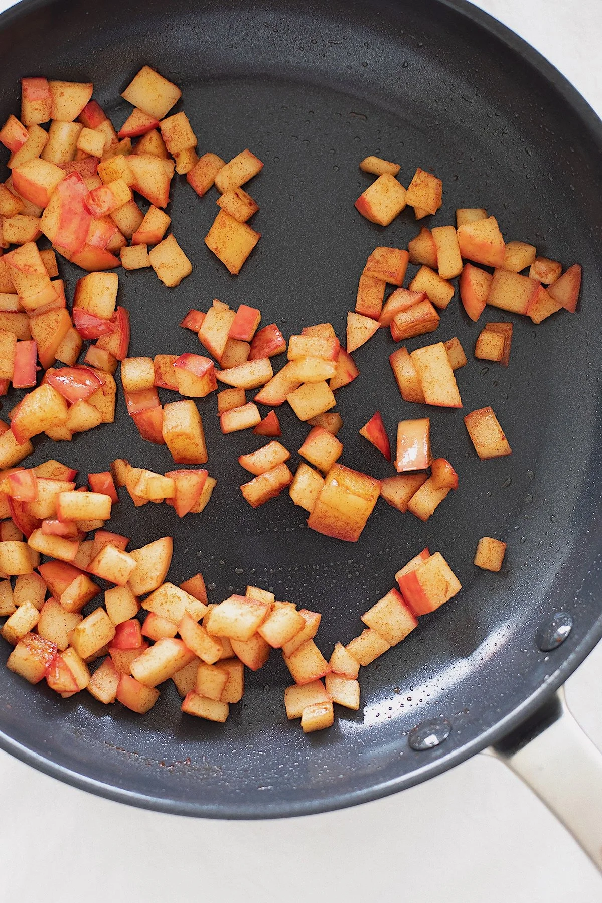 Diced apples sautéing in a skillet with cinnamon and coconut oil for chia pudding.