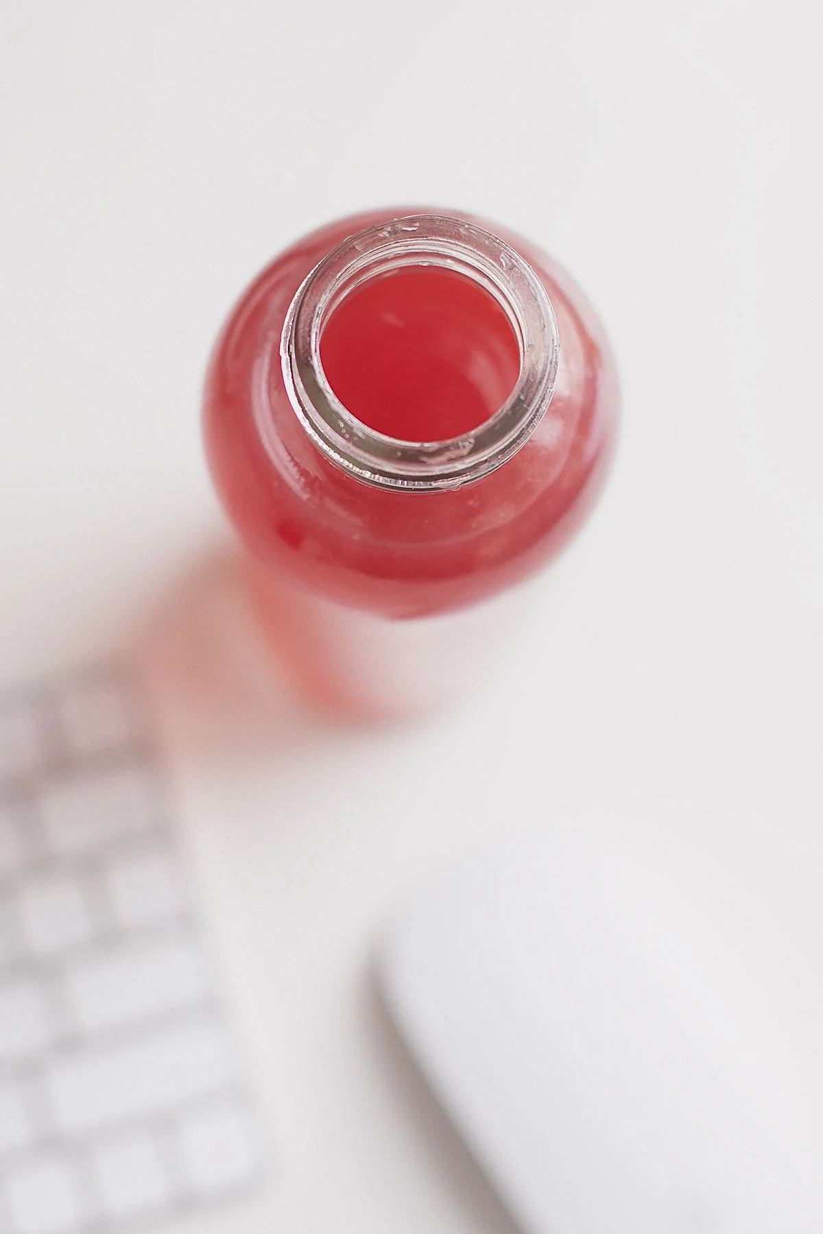 Open glass bottle of homemade electrolyte drink on a white desk.