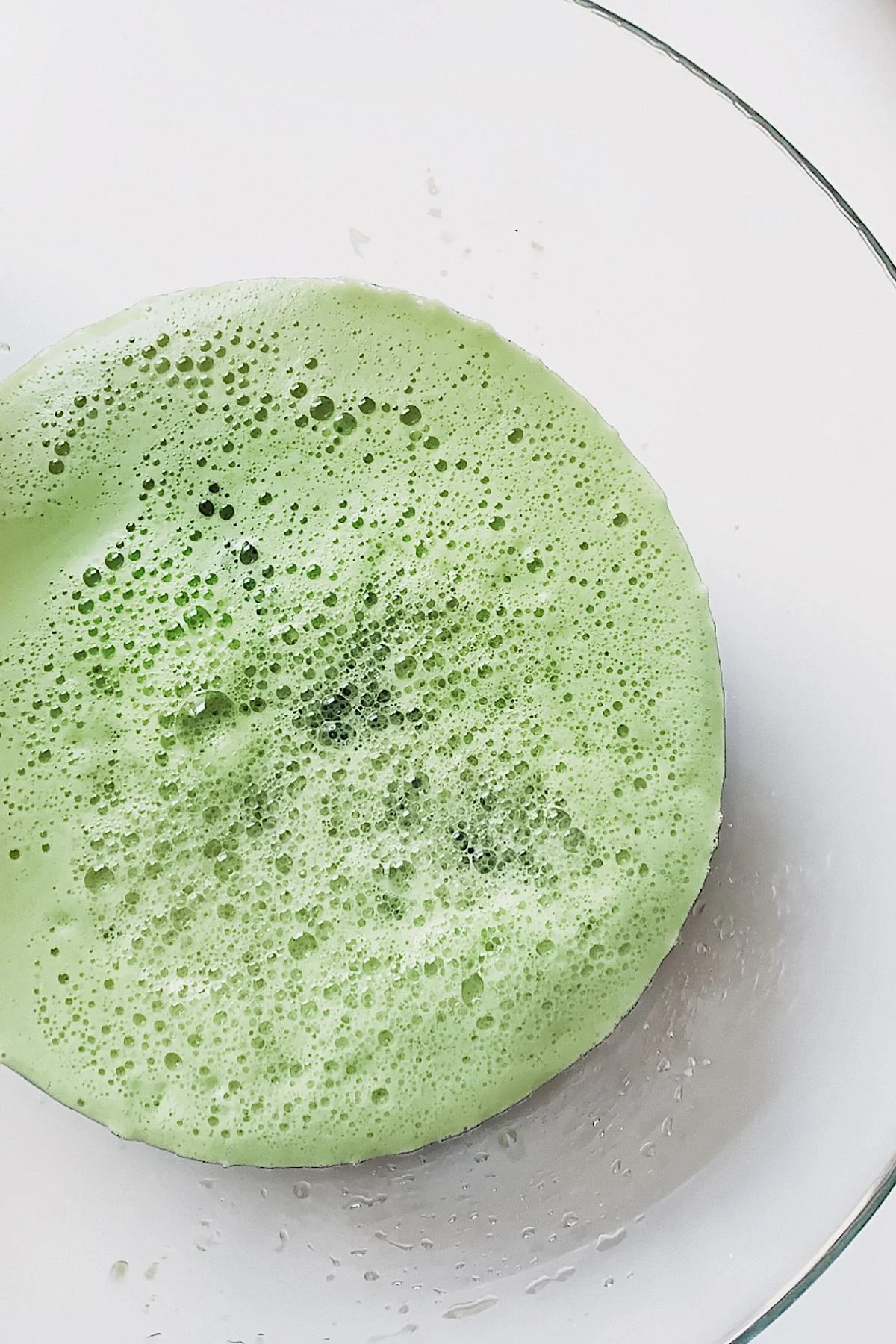 Green juice being strained through a nut milk bag over a bowl.
