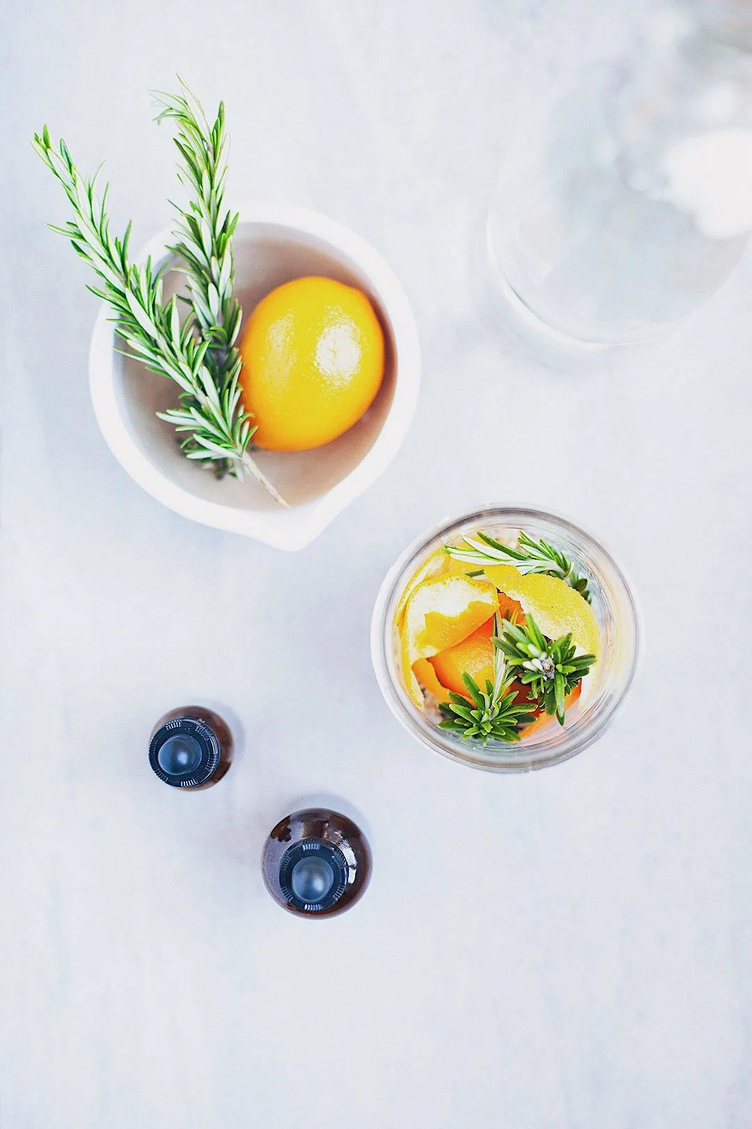 Flatlay of digestive bitters ingredients including lemon, rosemary, and glass bottles.