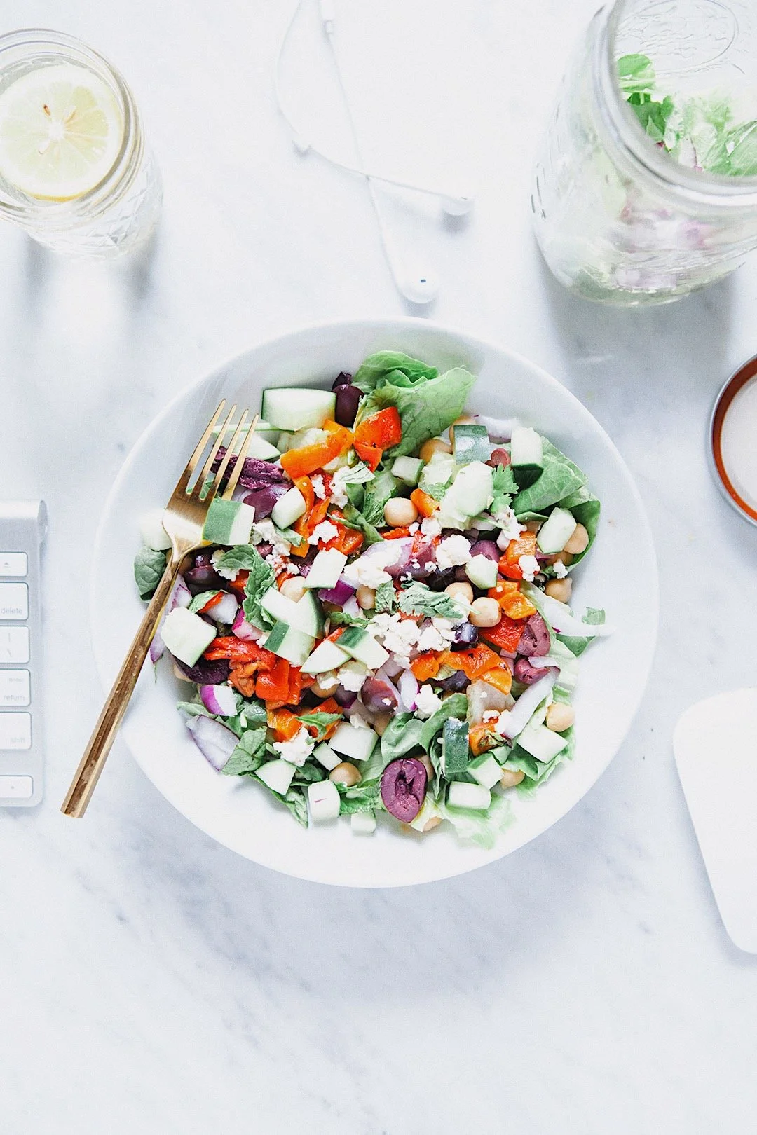 Prepared meal prep salad with greens, chickpeas, cucumber, olives, roasted peppers, and feta.