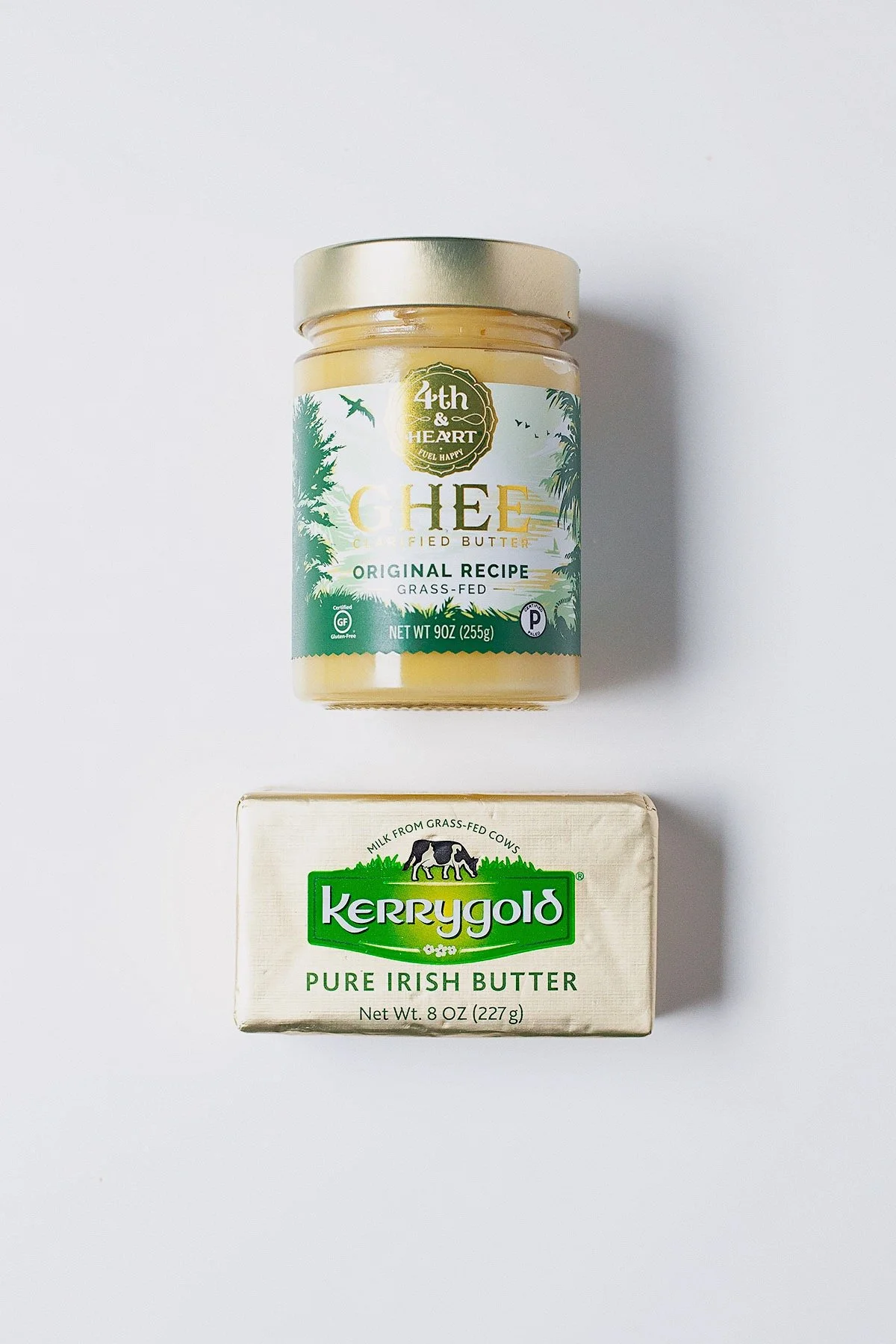 Jar of ghee and stick of grass-fed butter on a white background.
