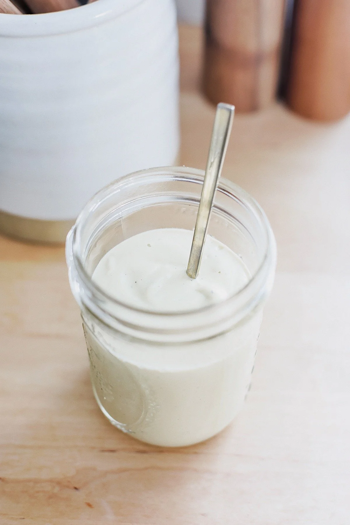 Close-up of creamy cashew alfredo sauce in glass jar with spoon, ready to serve.