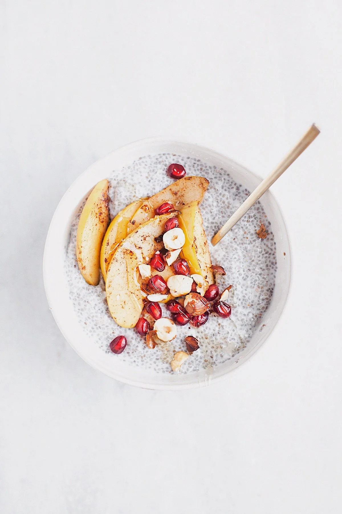 Cinnamon pear chia pudding topped with sautéed pears, pomegranate seeds, and chopped nuts in a white bowl.