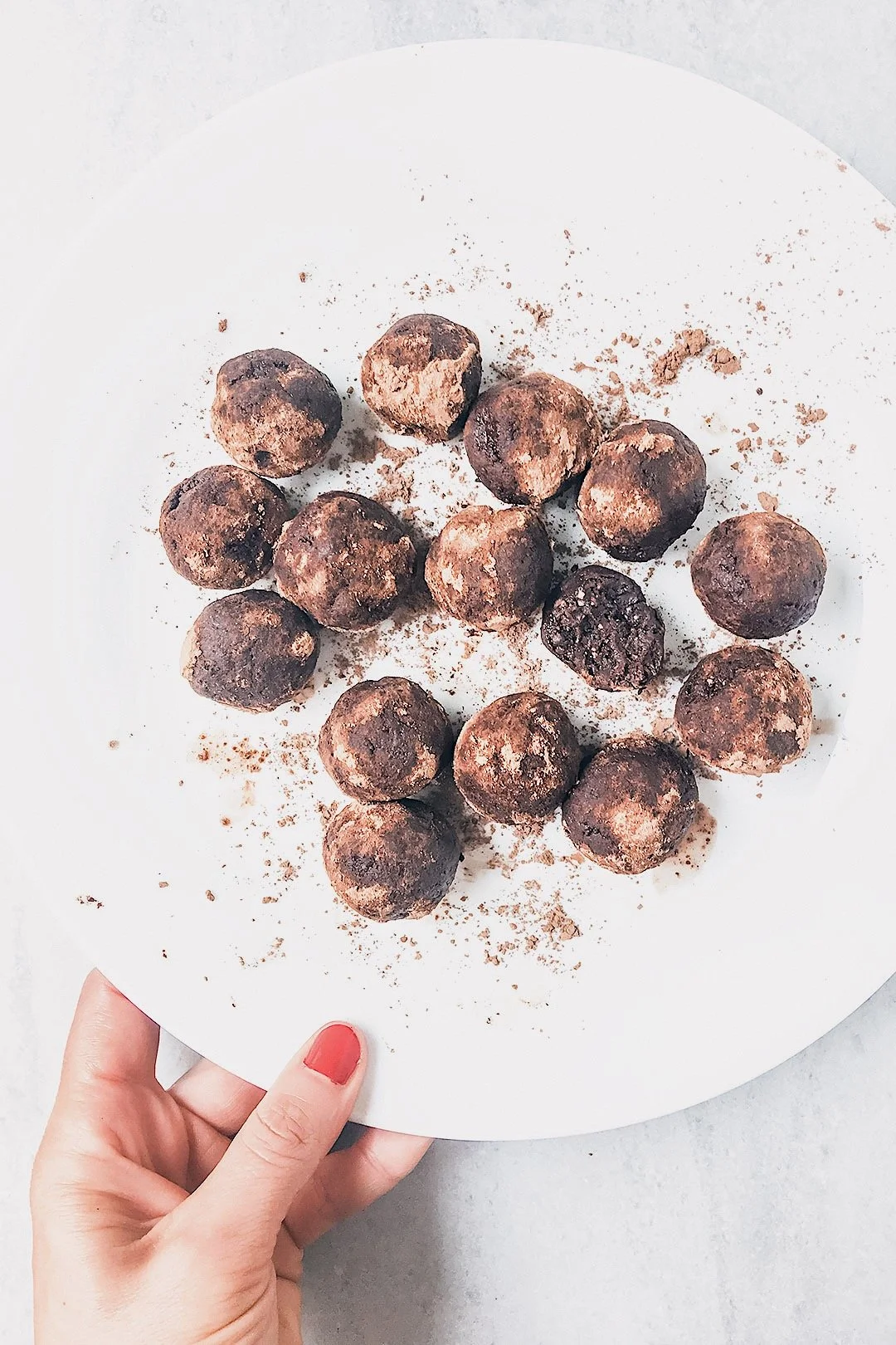 Vegan seed cycling brownie bites arranged on a white plate, dusted with cocoa powder.