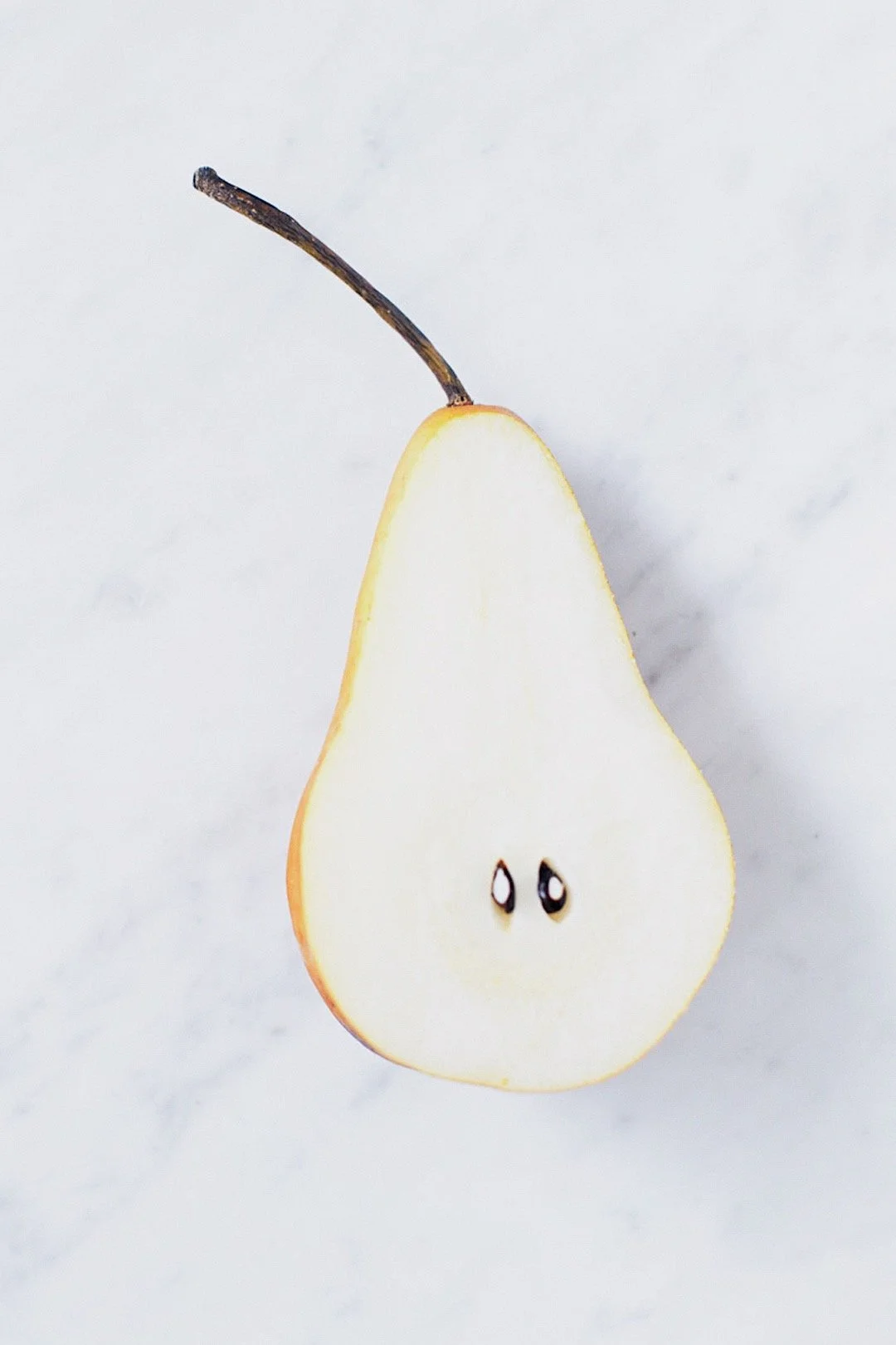 Halved pear on a white background, showing the simplicity of fresh ingredients used in cinnamon pear chia pudding.