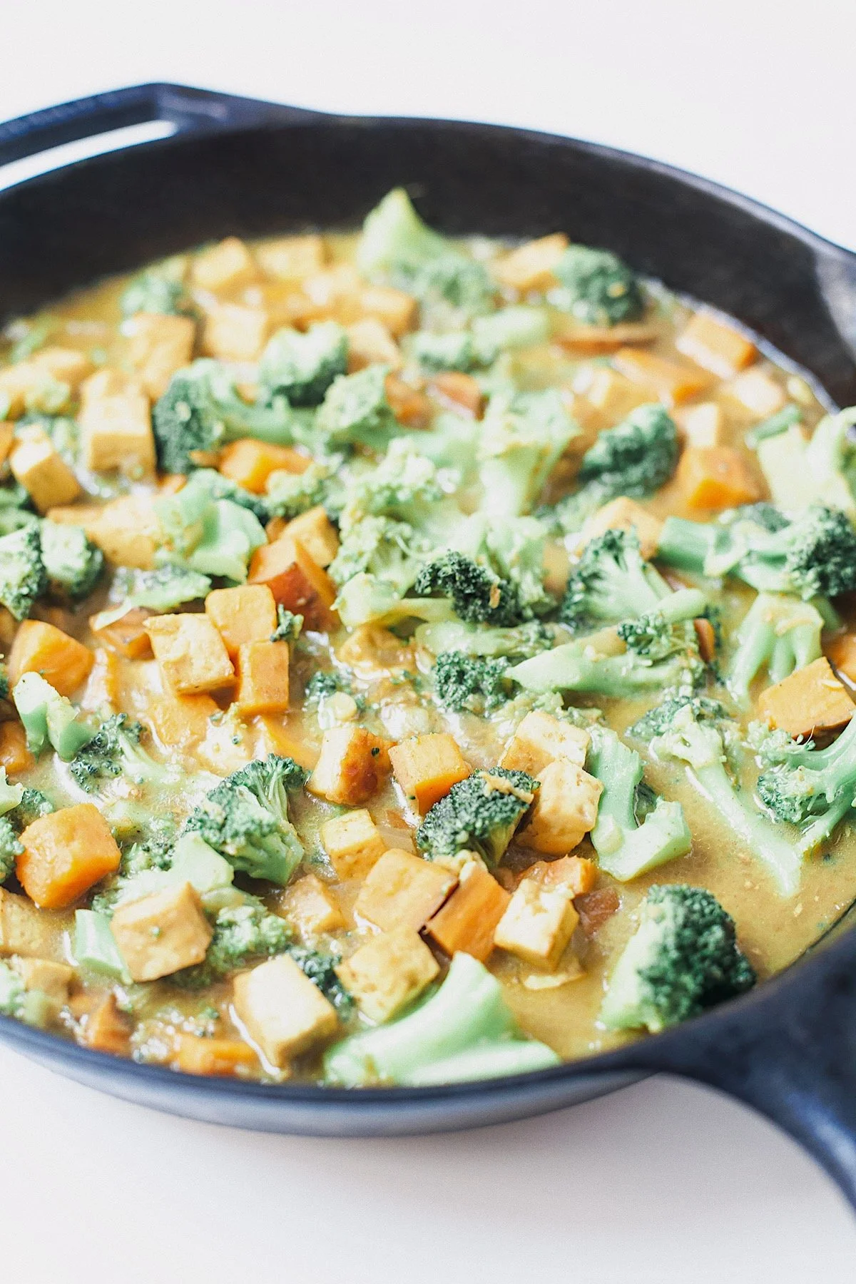 Coconut curry with broccoli, sweet potato, and tofu cooking in a cast-iron skillet.