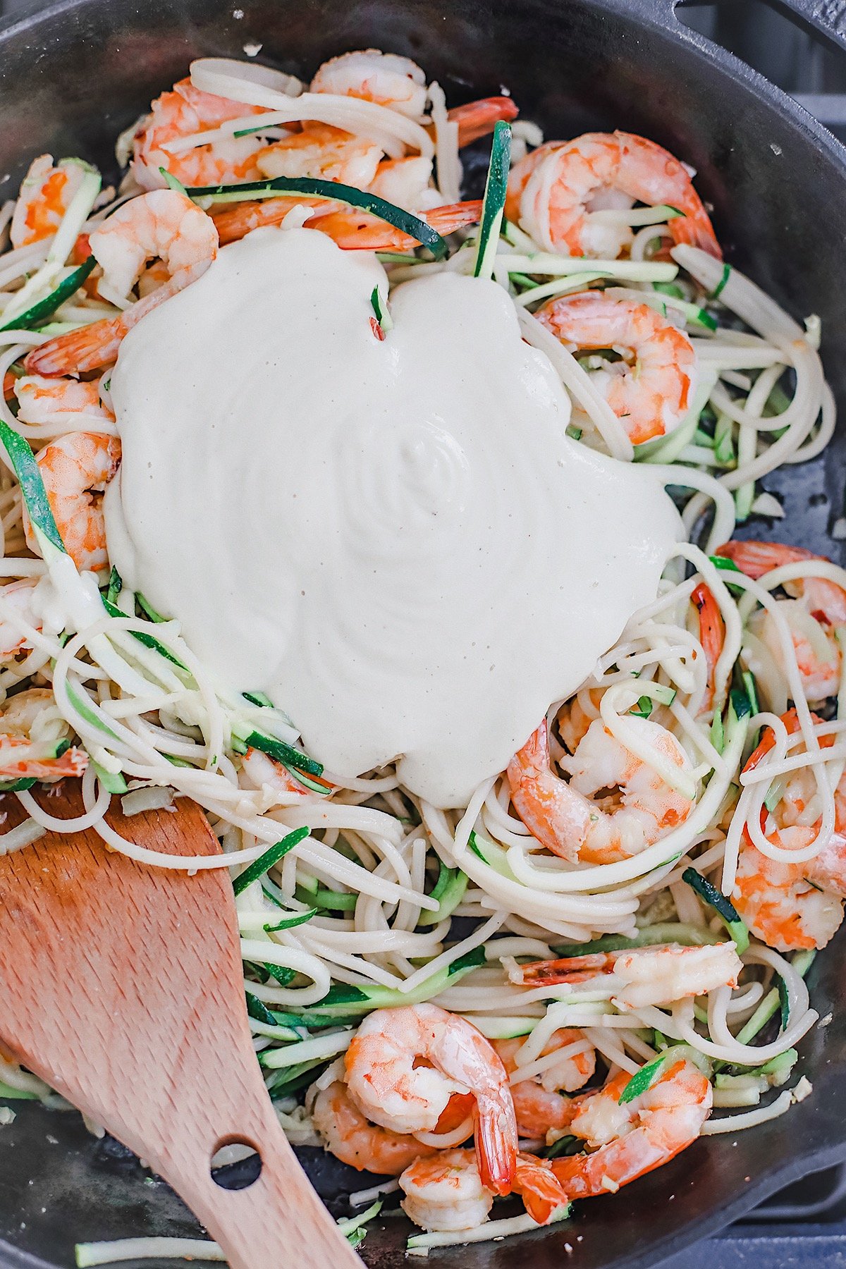 Shrimp and zucchini noodles topped with cashew alfredo sauce in a black skillet.