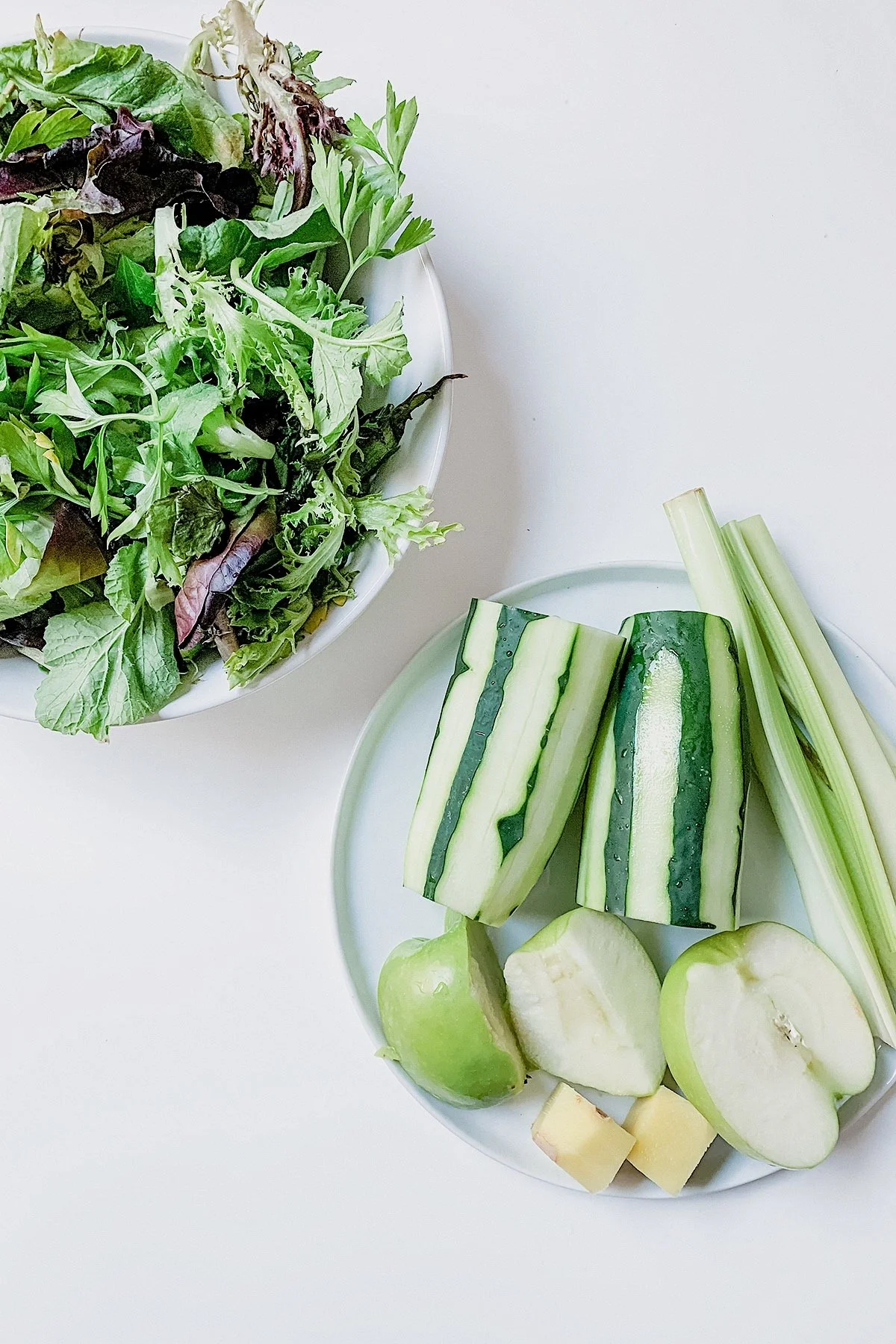 Cucumber, celery, apple, lemon, and greens on a white surface.