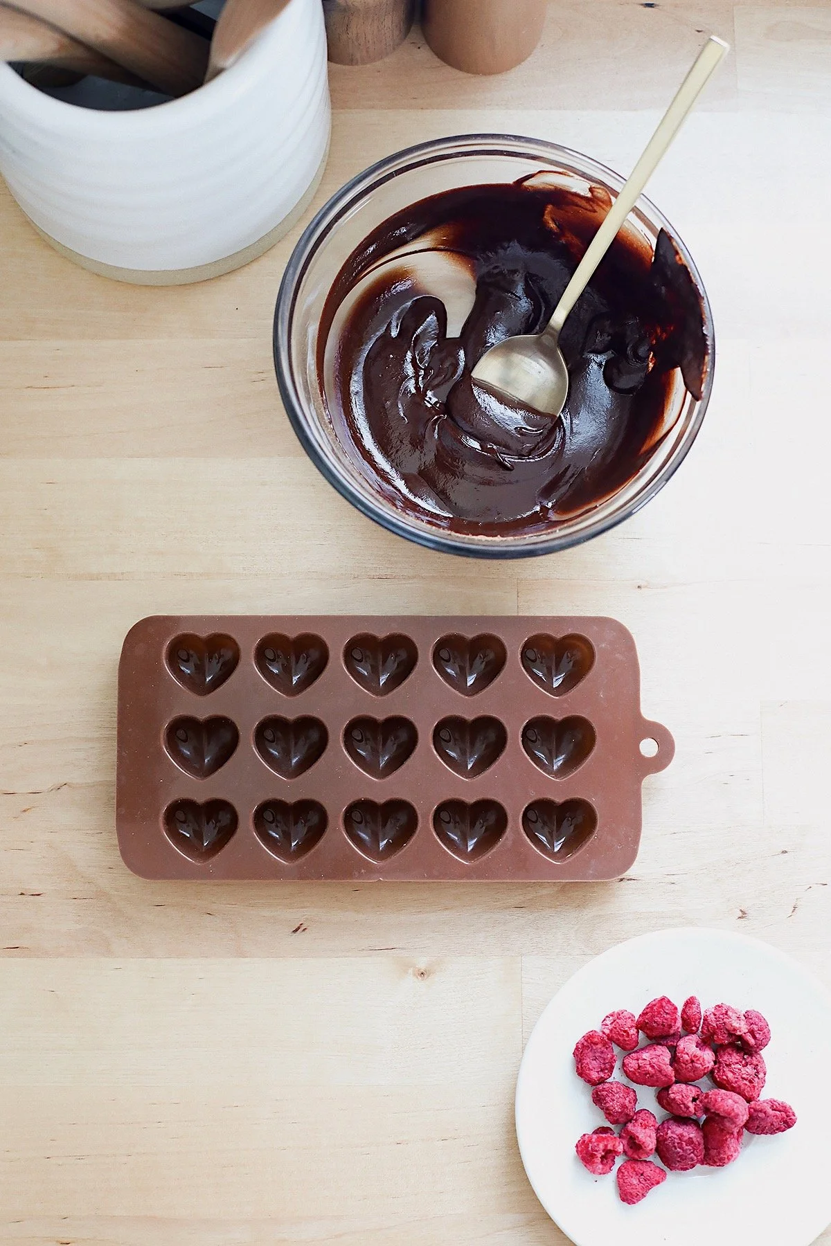 Melted homemade chocolate being spooned into silicone heart mold with raspberries.