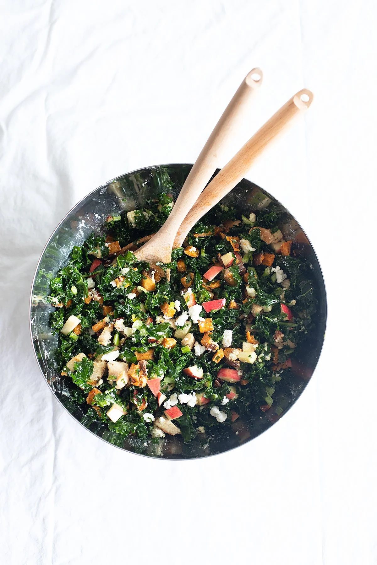 Fall kale and apple salad with roasted sweet potatoes, apples, pecans, chicken, and feta in a large bowl.