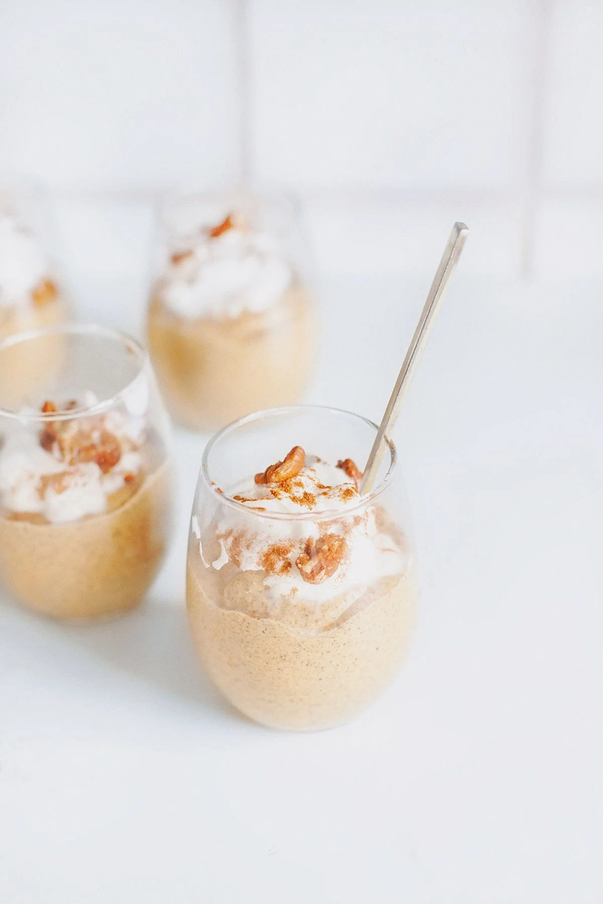 Creamy pumpkin chia hemp seed pudding in small glasses topped with coconut whipped cream and pecans.