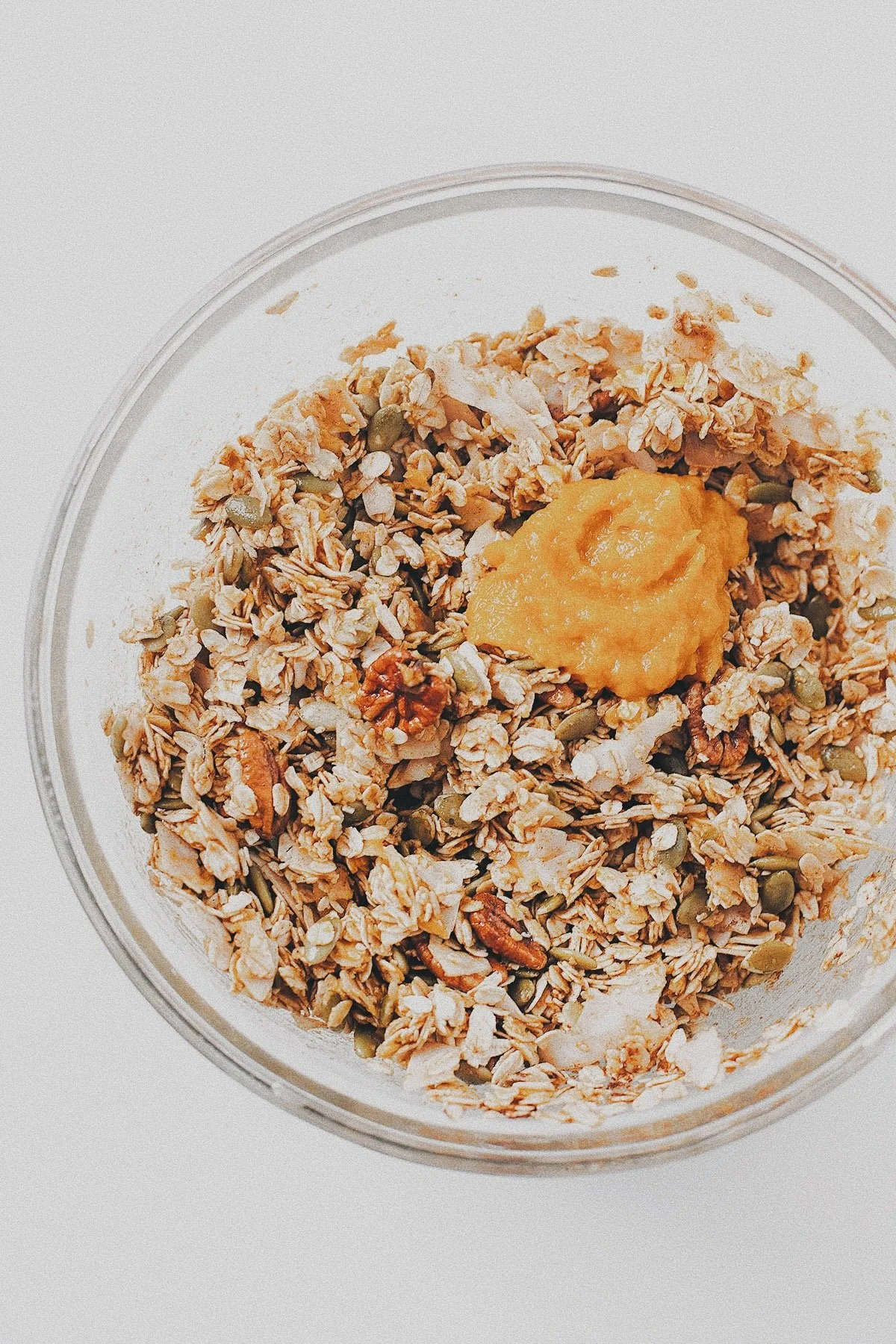 Rolled oats, nuts, seeds, coconut, and pumpkin purée being mixed for homemade pumpkin granola.