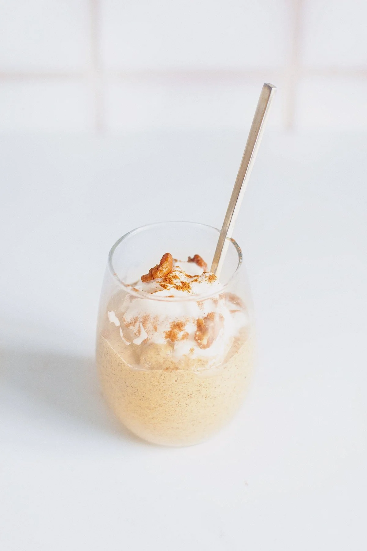 Single glass of pumpkin chia hemp seed pudding with spoon, topped with coconut cream and cinnamon.