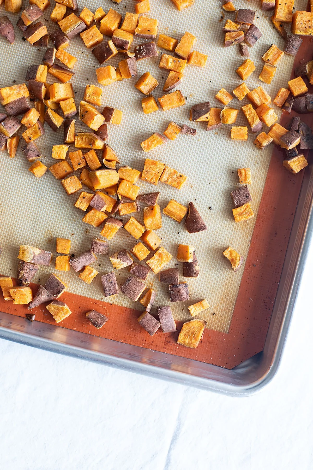 Roasted sweet potato cubes on a sheet pan for fall kale and apple salad.