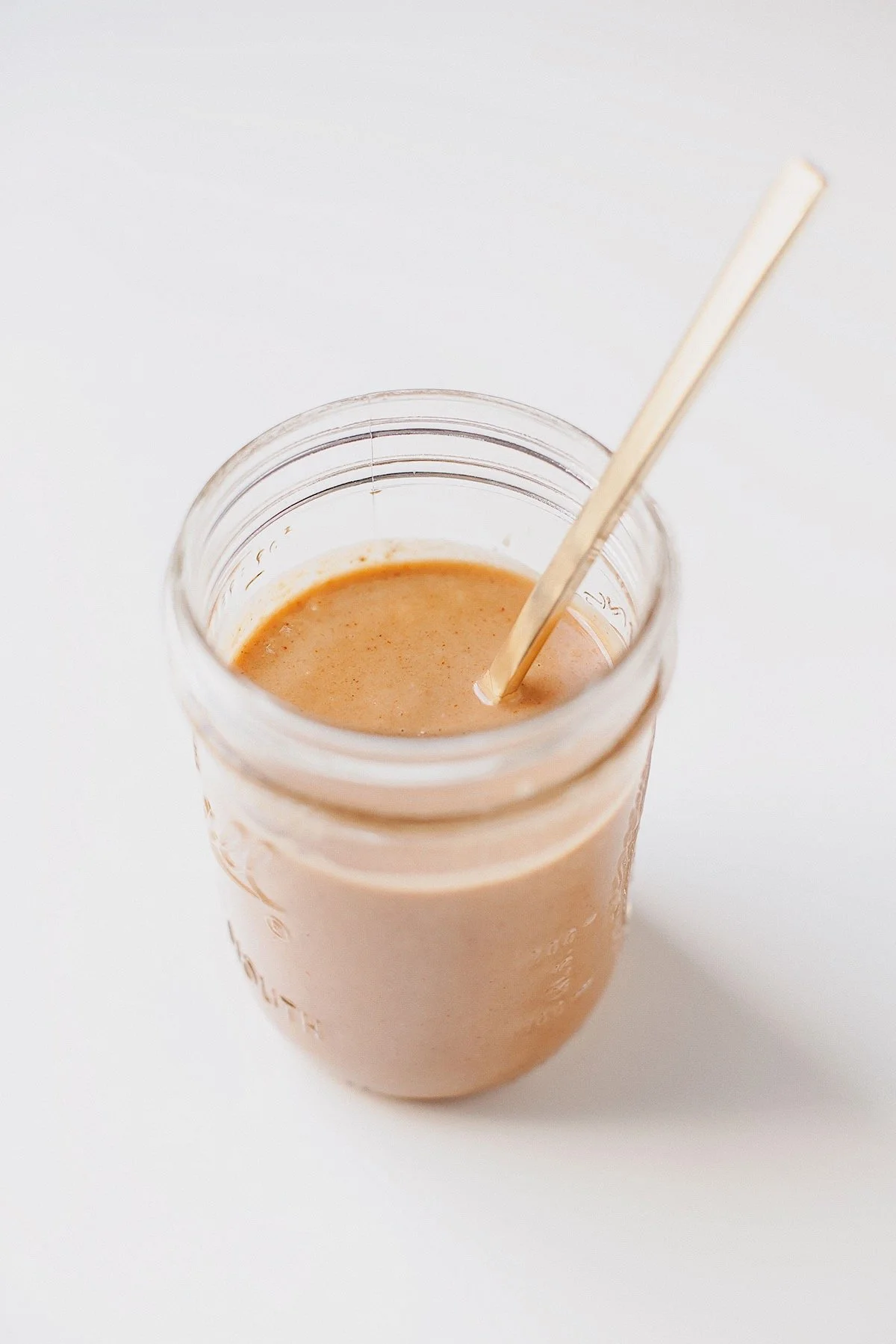 Coconut peanut sauce in a glass jar with spoon on white background.