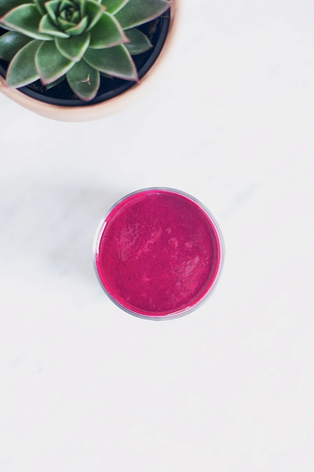 Vibrant purple blueberry and beet smoothie in a glass on a white surface.