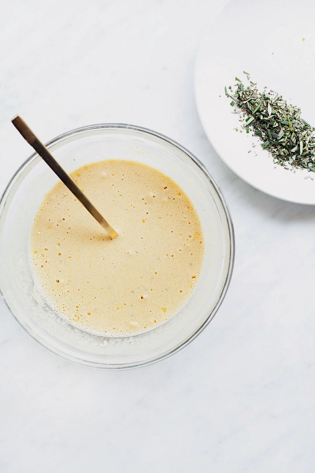 Chickpea flour batter for socca in a bowl with fresh rosemary and olive oil.