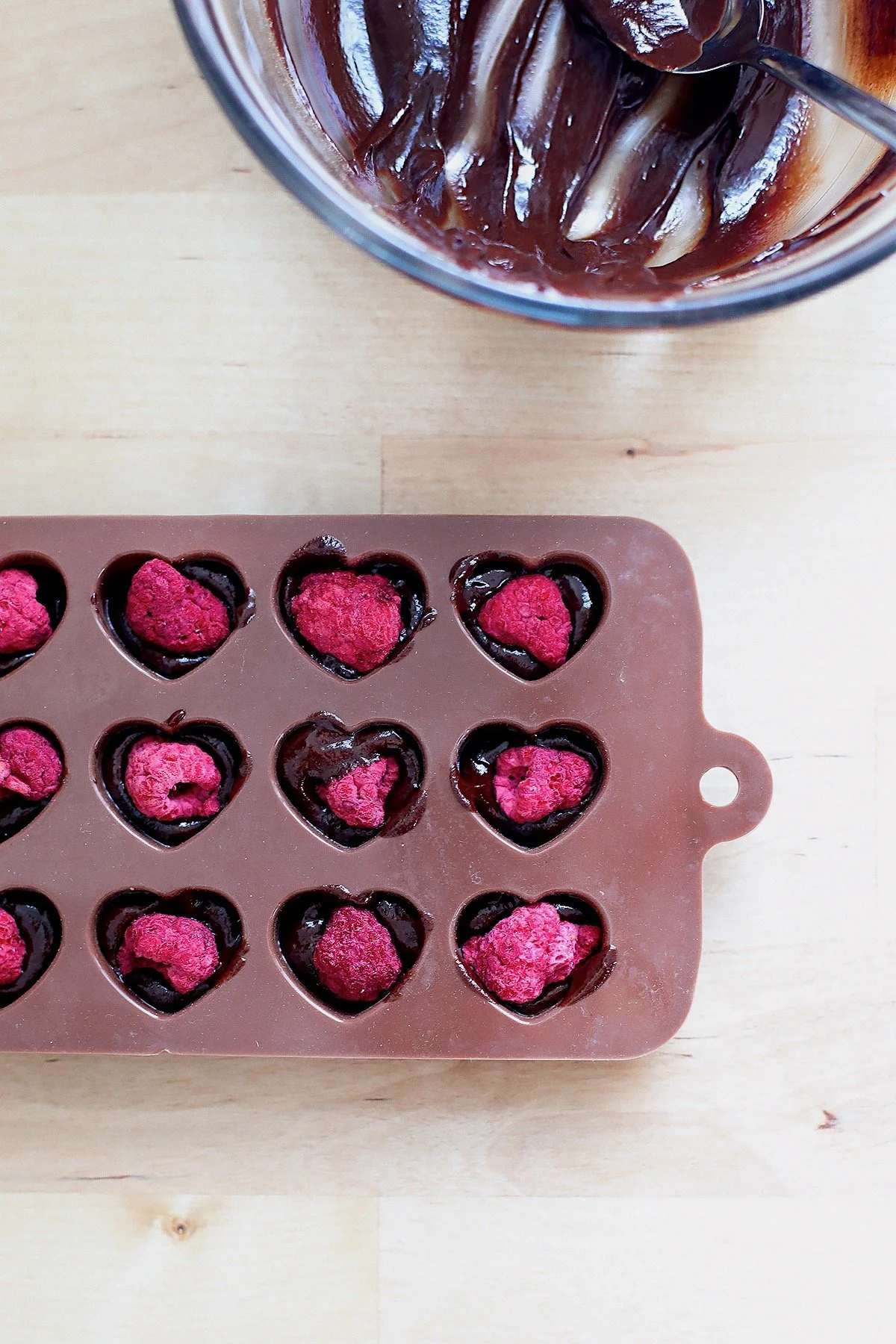 Silicone heart mold filled with homemade chocolate and raspberries before freezing.