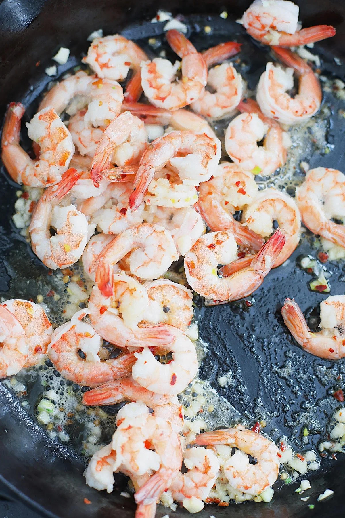 Shrimp cooking in a cast-iron skillet with olive oil and garlic.