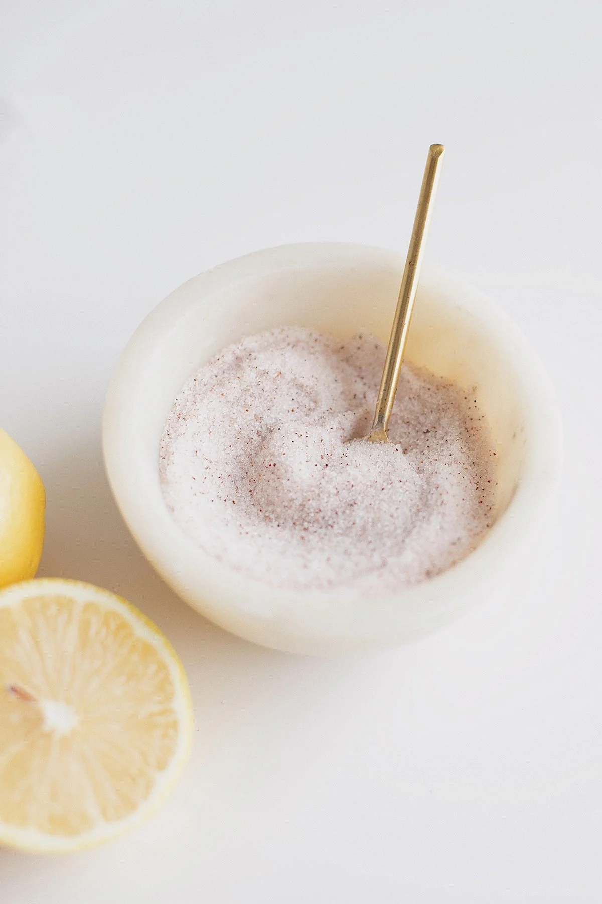 Close-up of pink mineral salt in a white bowl with a gold spoon.
