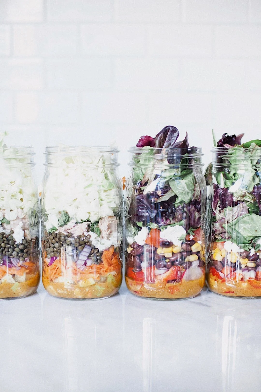 Several mason jar salads packed with dressing, vegetables, beans, cheese, and greens for the week.