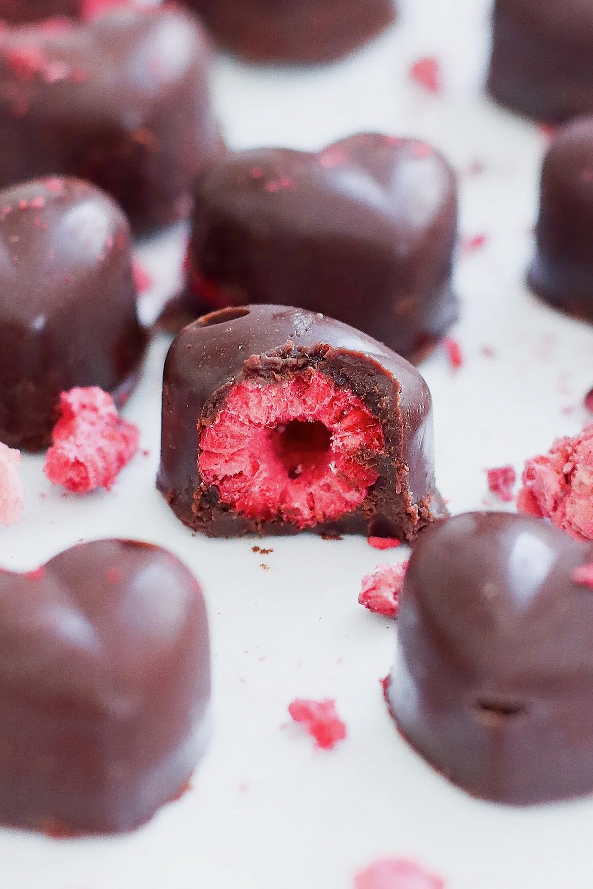 Close-up of homemade raspberry chocolate with bite taken out, showing freeze-dried raspberry center and dark chocolate coating.