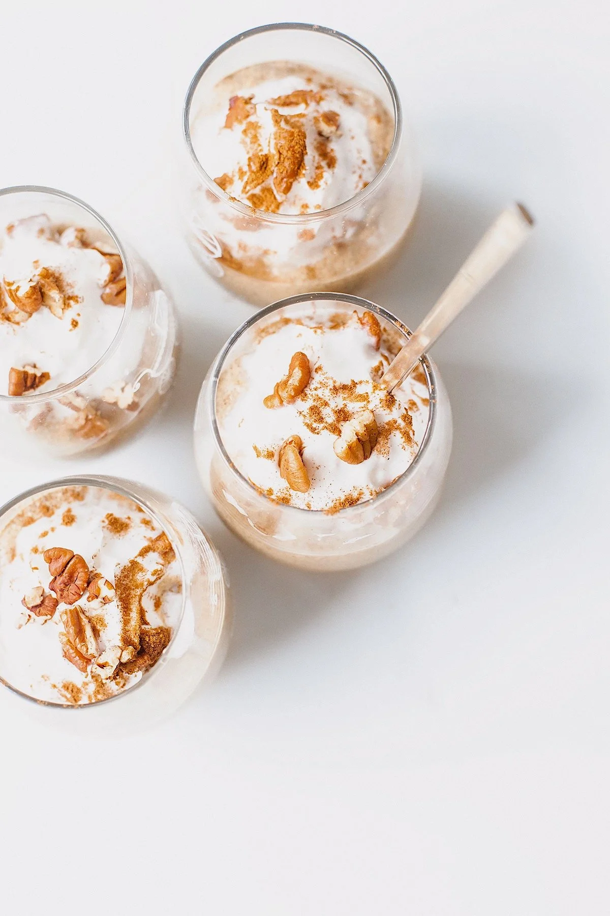 Overhead view of four pumpkin chia hemp seed puddings topped with whipped coconut cream, pecans, and cinnamon.