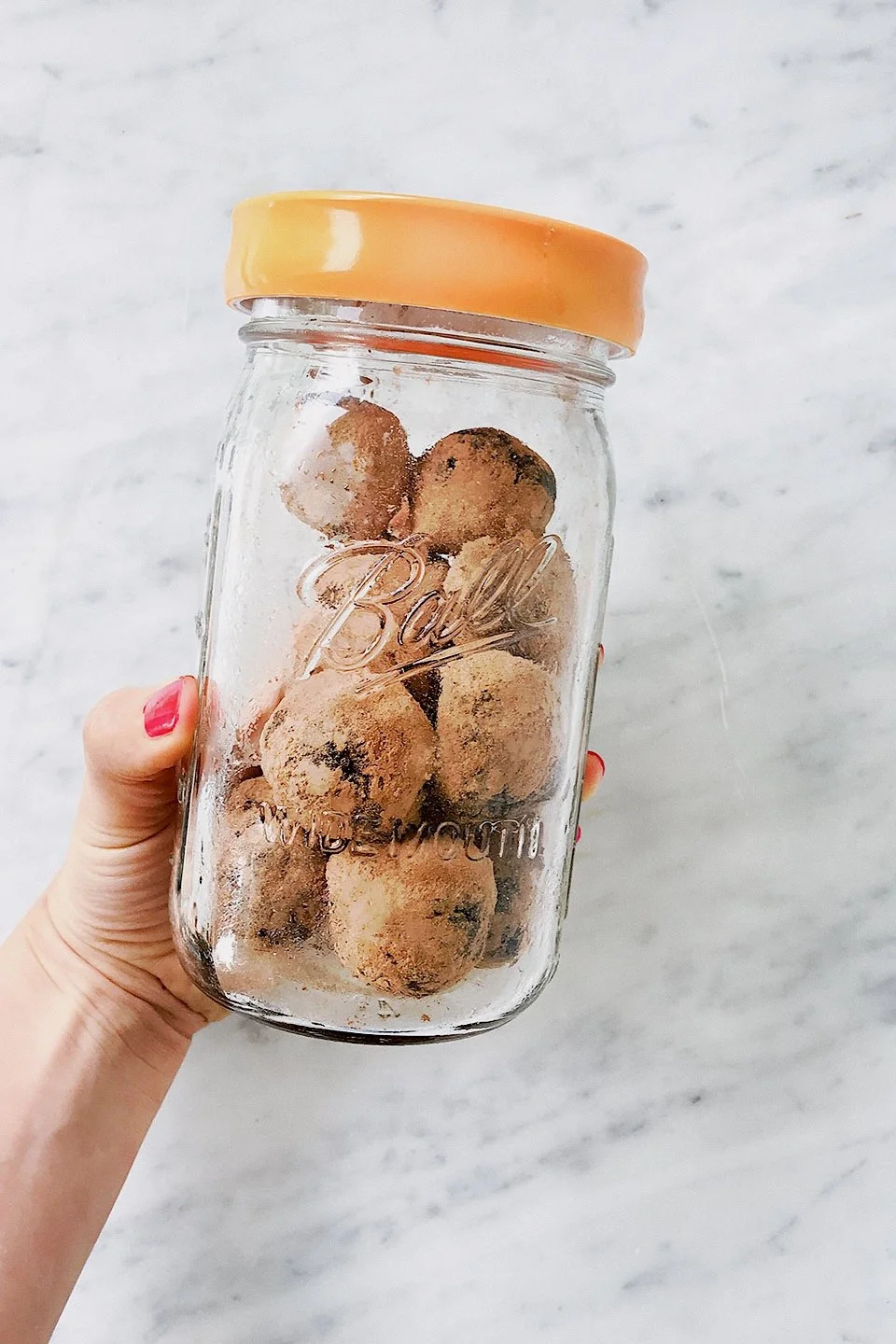 Hand holding a jar of seed cycling bites for supporting estrogen and progesterone balance.