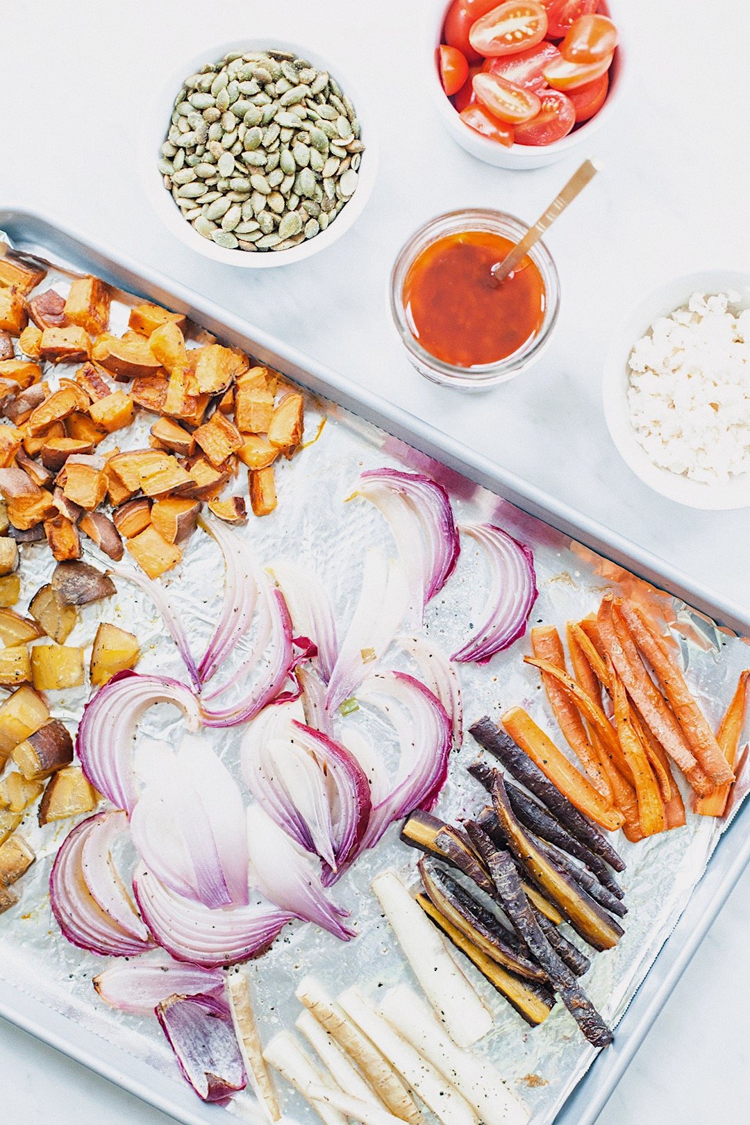 Roasted sweet potatoes, carrots, onions, tomatoes, feta, and dressing prepared for meal prep salads.