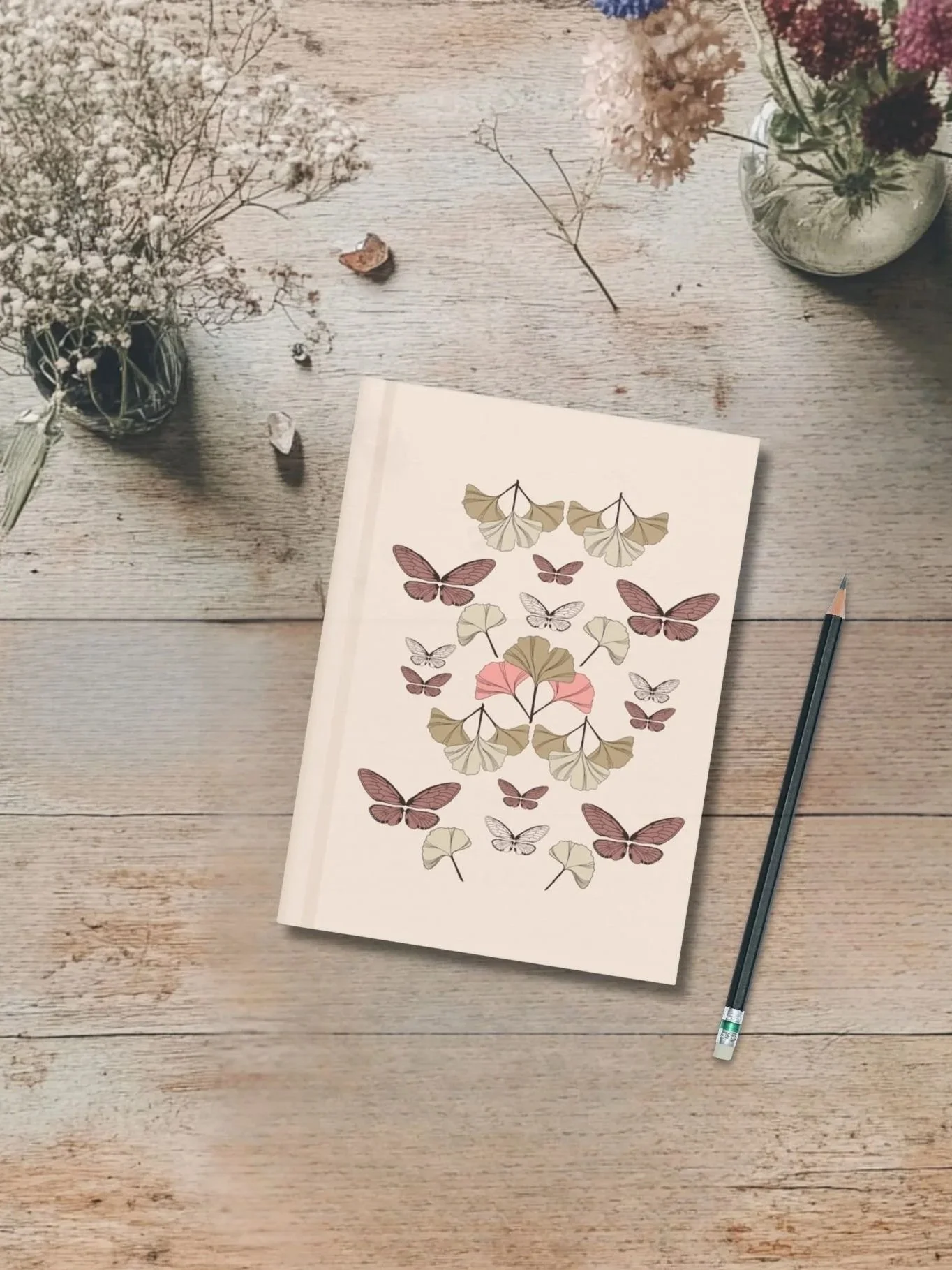 Flat lay of Ginkgo and Wing botanical journal with butterfly pattern, displayed on rustic wood desk with pencil, dried flowers, and nature elements.