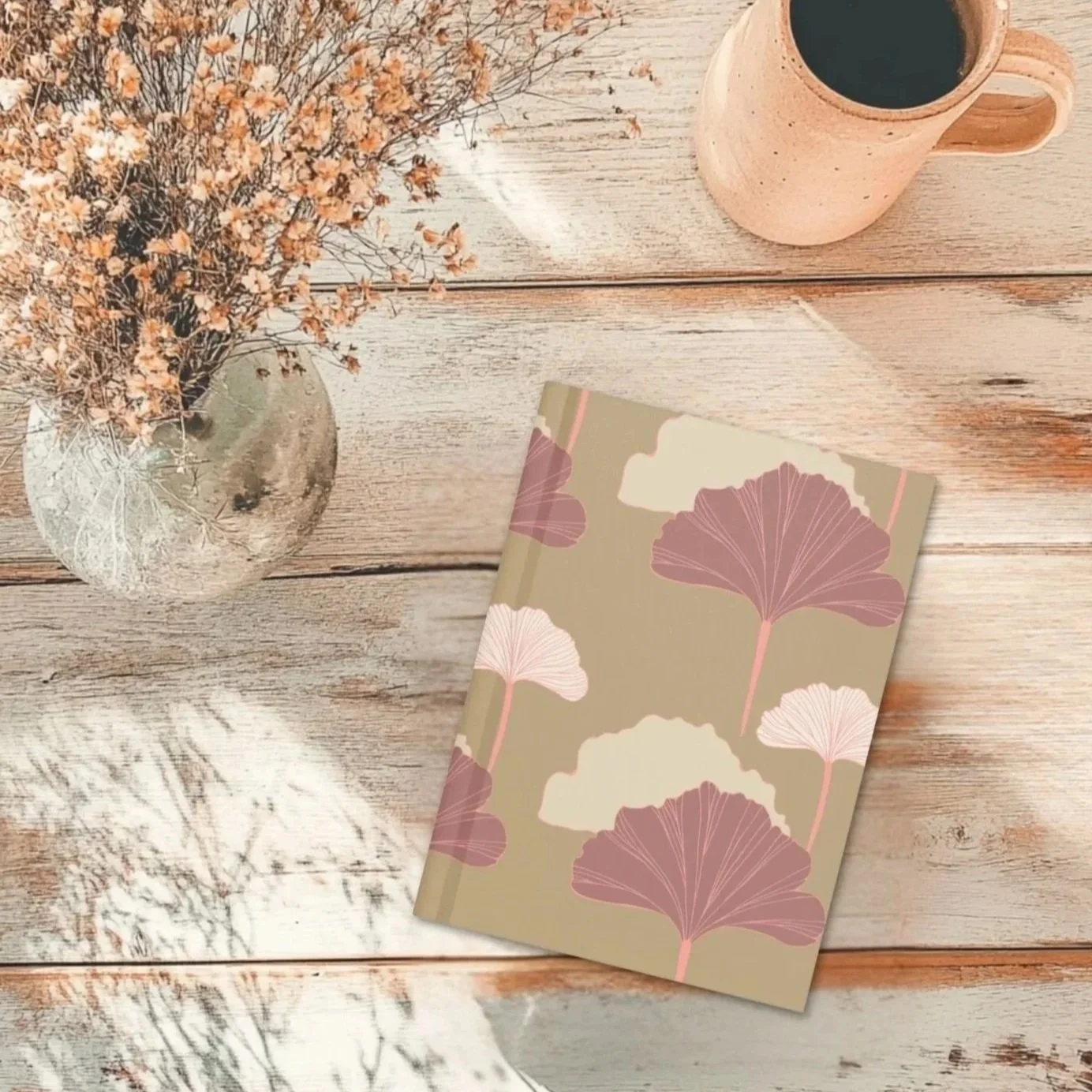 Flat lay of the Blush Canopy ginkgo journal beside dried flowers and a ceramic mug on a rustic wood surface