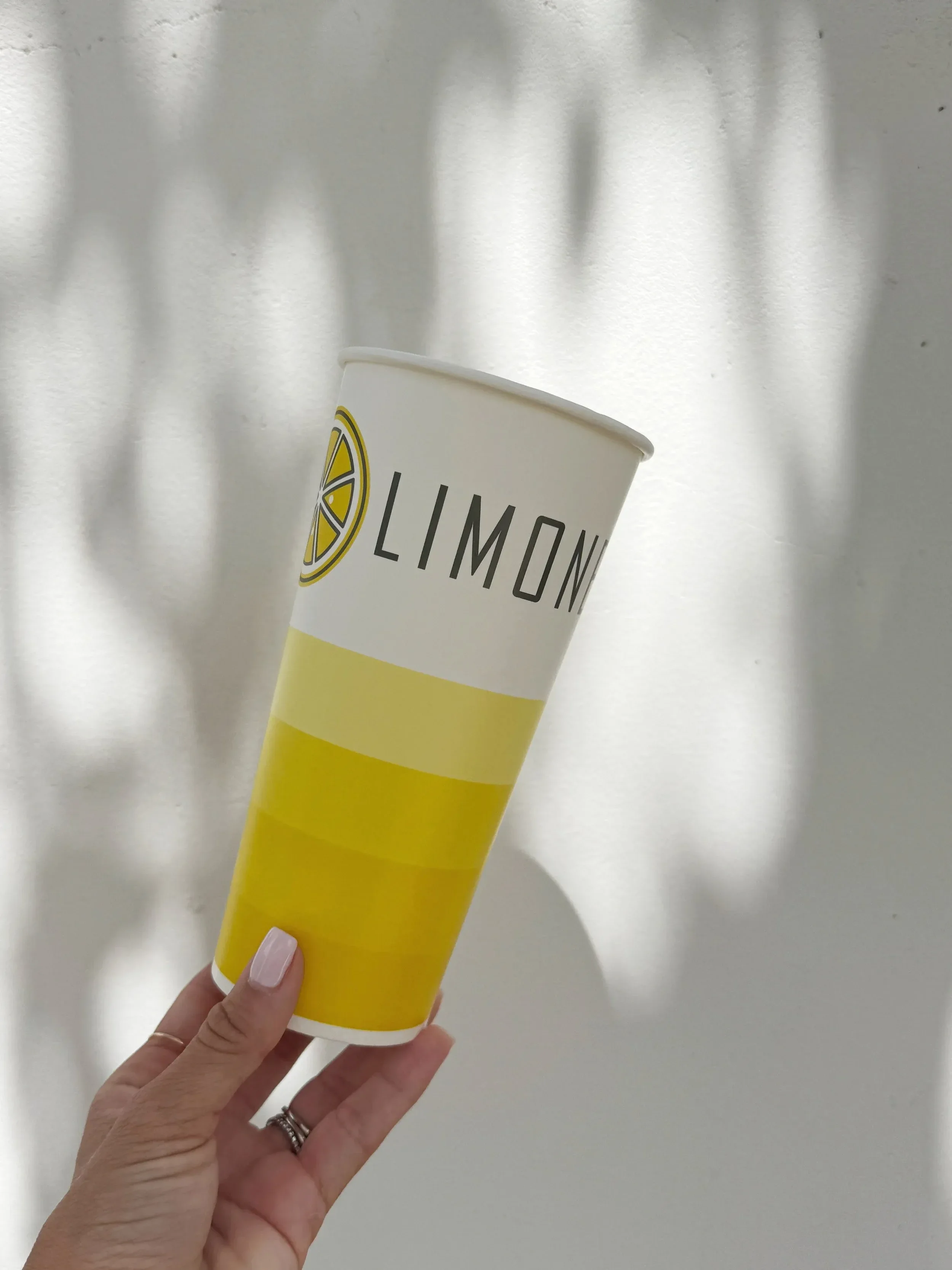 A person holding a lemon-themed paper cup with the text 'LIMON' and a lemon slice graphic, against a plain white background.