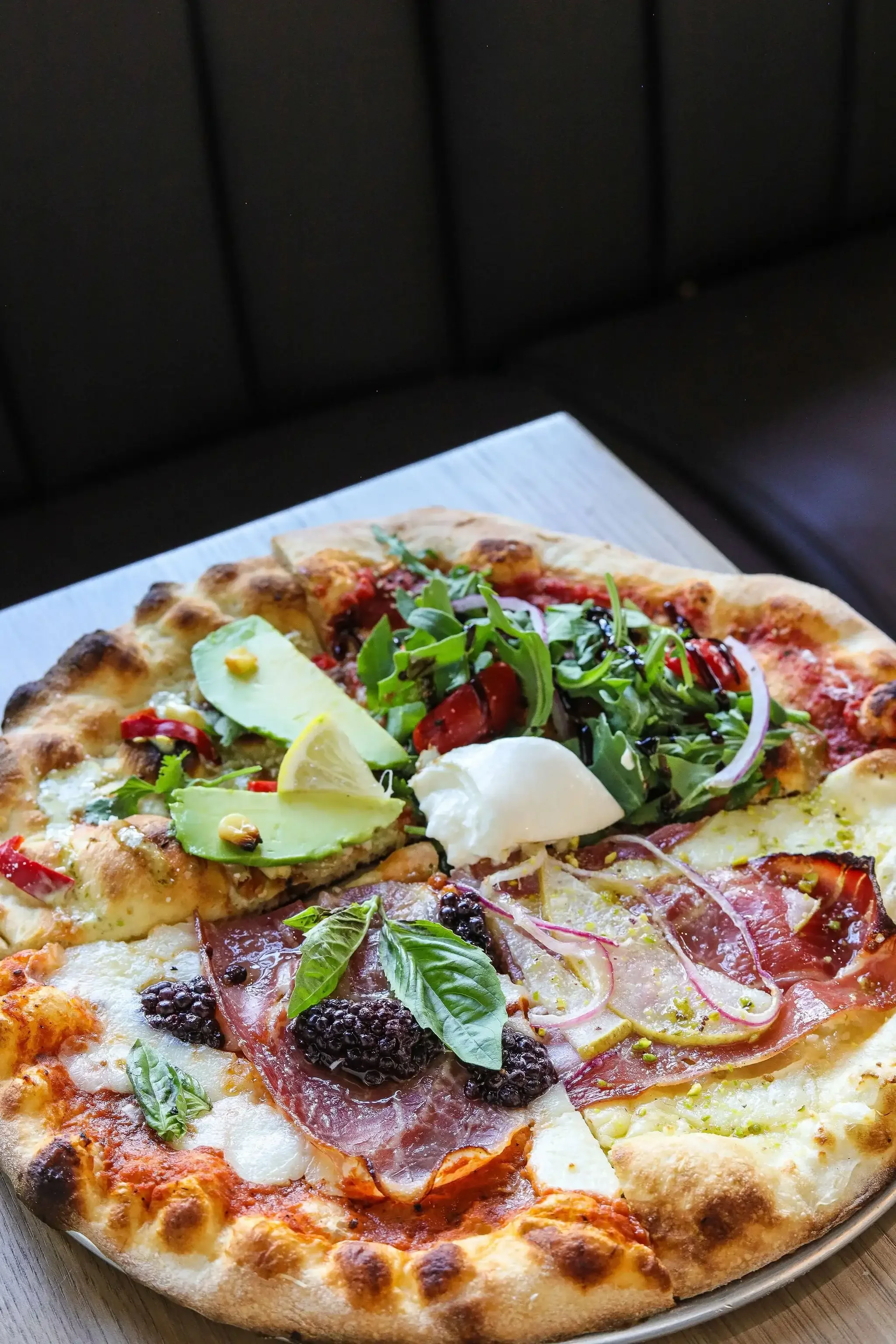 Assorted slices of pizza with various toppings including pepperoni, fresh basil, arugula, blackberries, cheese, and vegetables, on a round tray