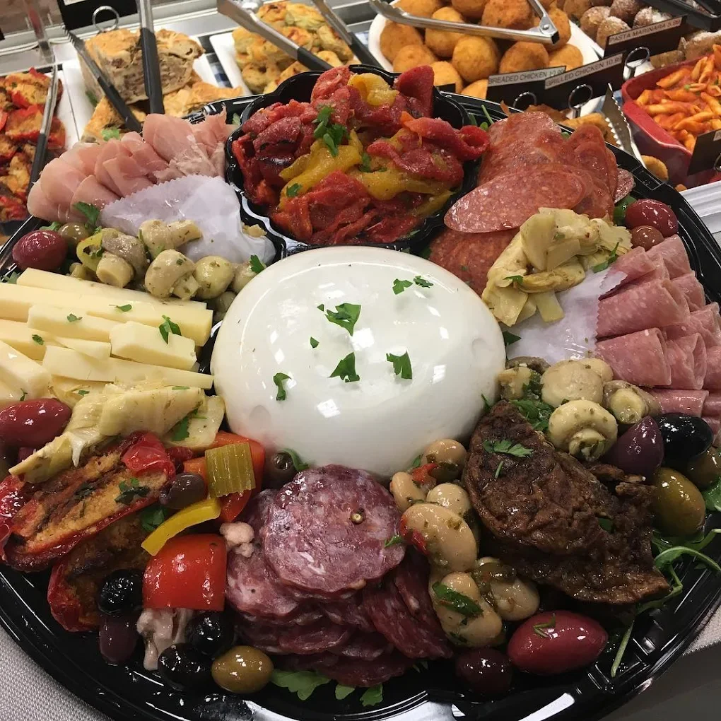 A platter of assorted cheeses, cured meats, marinated vegetables, and olives, with a central ball of mozzarella cheese garnished with herbs.