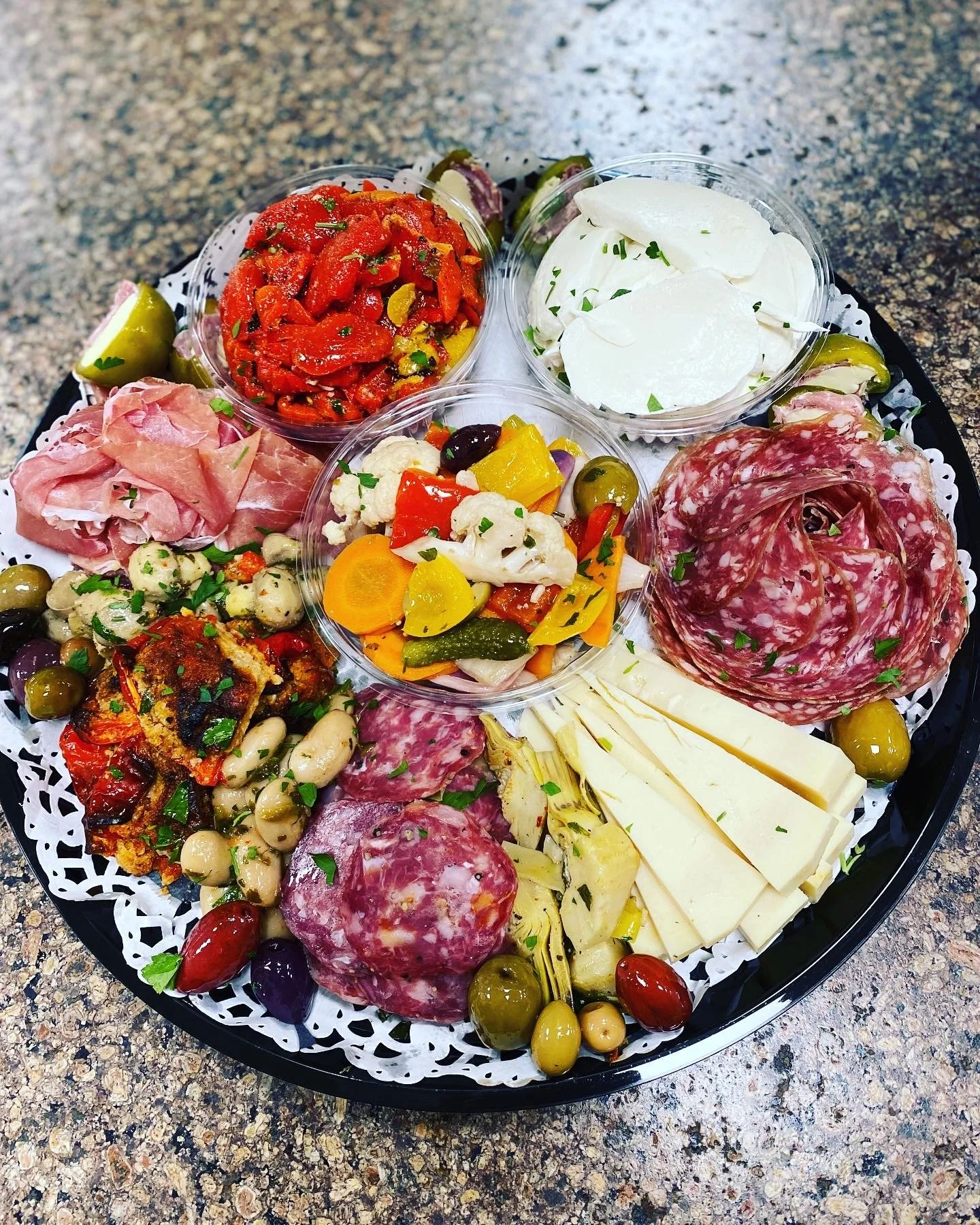A charcuterie tray with various cheeses, cured meats, marinated vegetables, fresh vegetables, and olives.