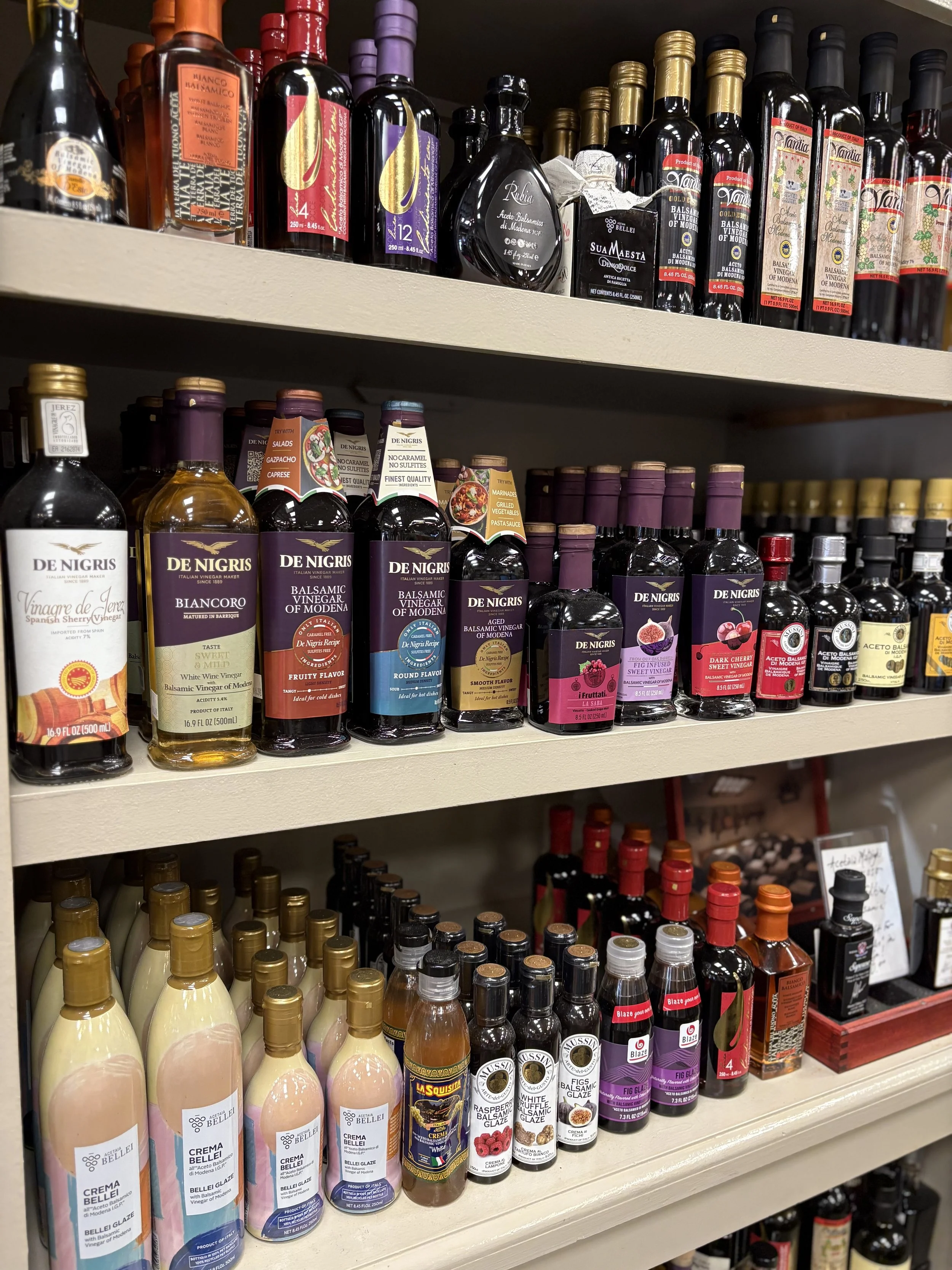 Shelves filled with various bottles of vinegar, balsamic glaze, and salad dressings in a store.