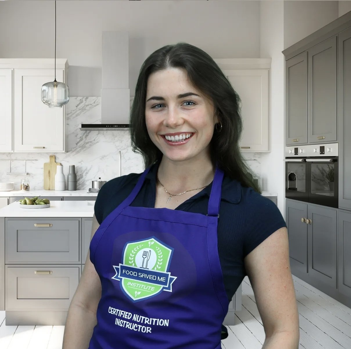 A smiling woman with dark hair standing in a modern kitchen wearing a purple apron with a food safety logo and the text "Food Saved Me Institute, Certified Nutrition Instructor".