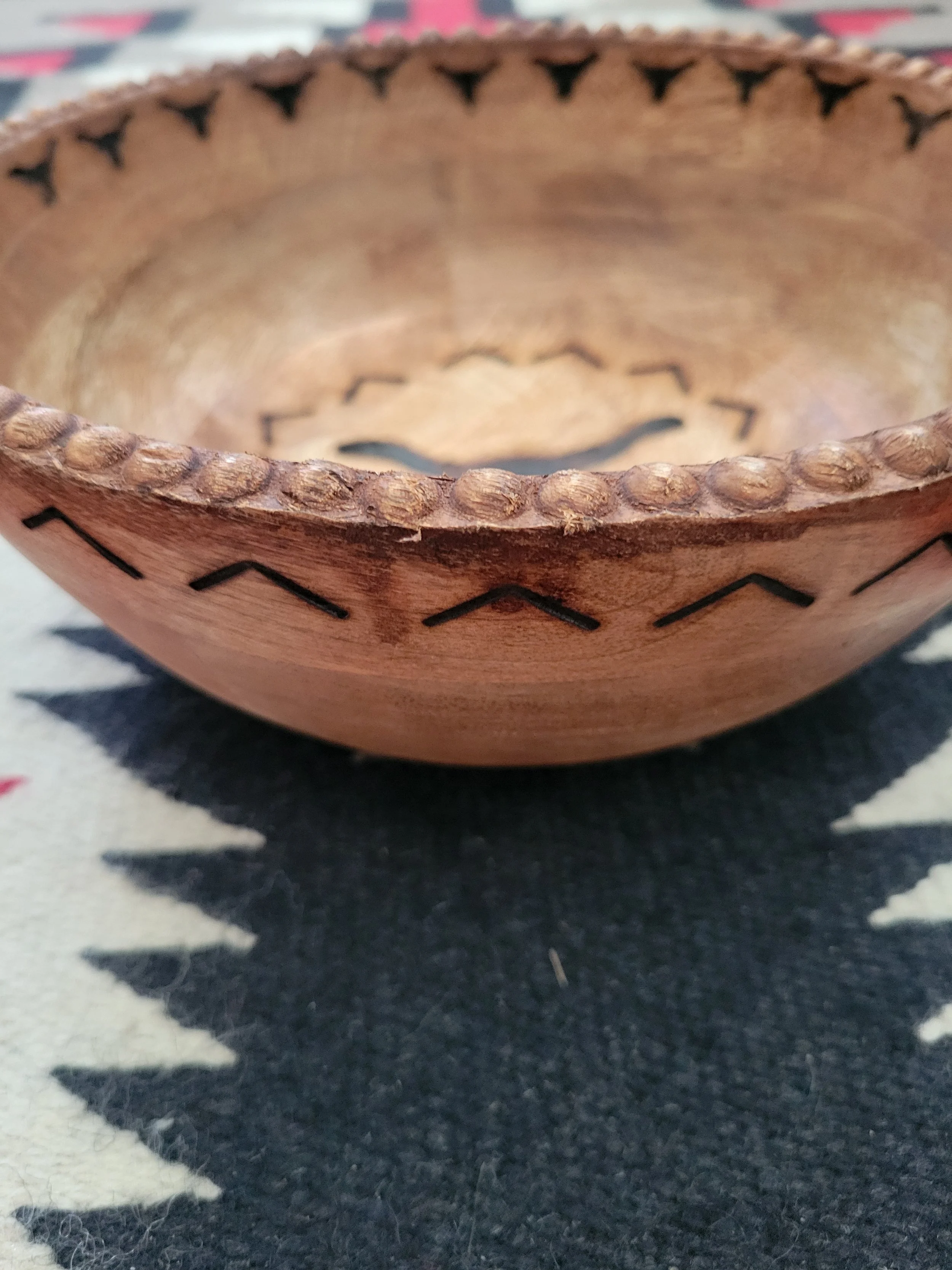 Wooden bowl with carved and stamped design, resting on a black and white patterned fabric surface.