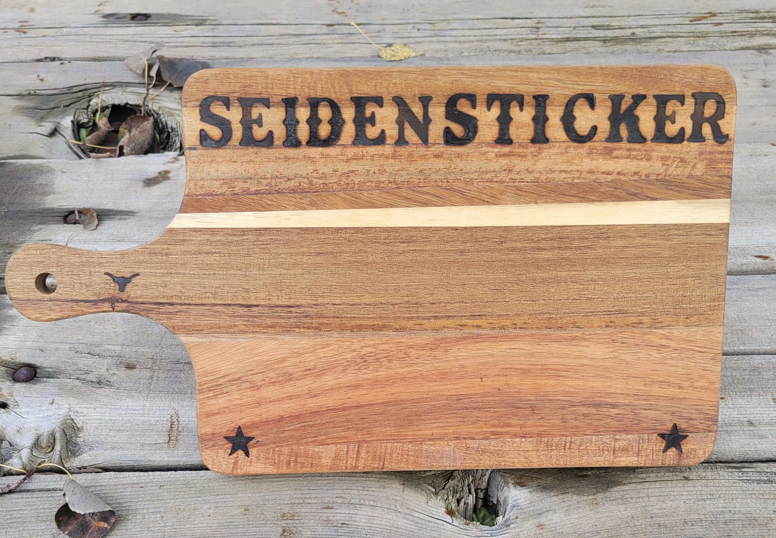 Wooden serving cutting board with the word 'SEIDENSTICKER' engraved at the top, resting on a weathered wooden surface.