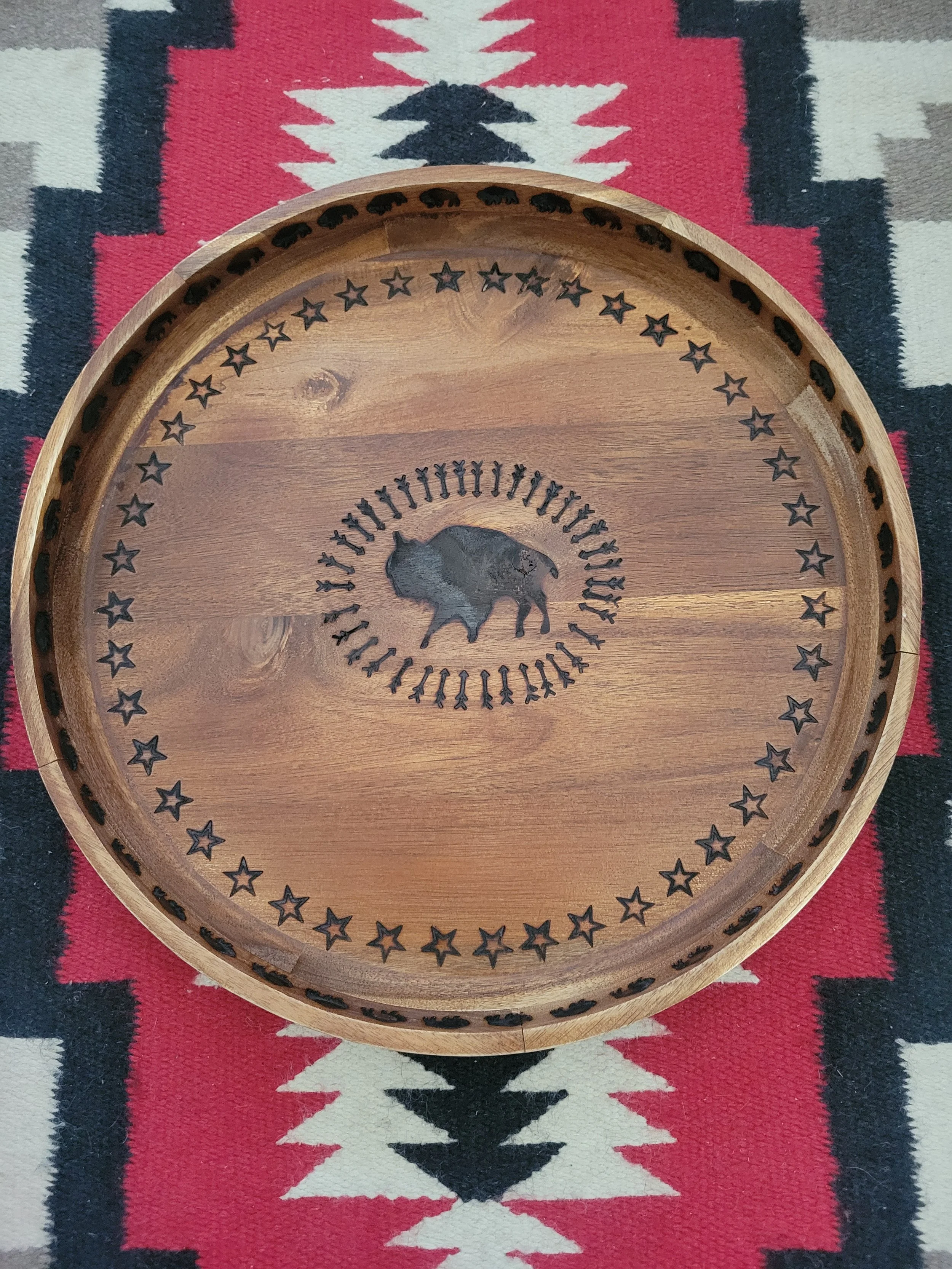 Round wooden tray with black buffalo design in the center, surrounded by stars, on a Southwestern patterned rug.