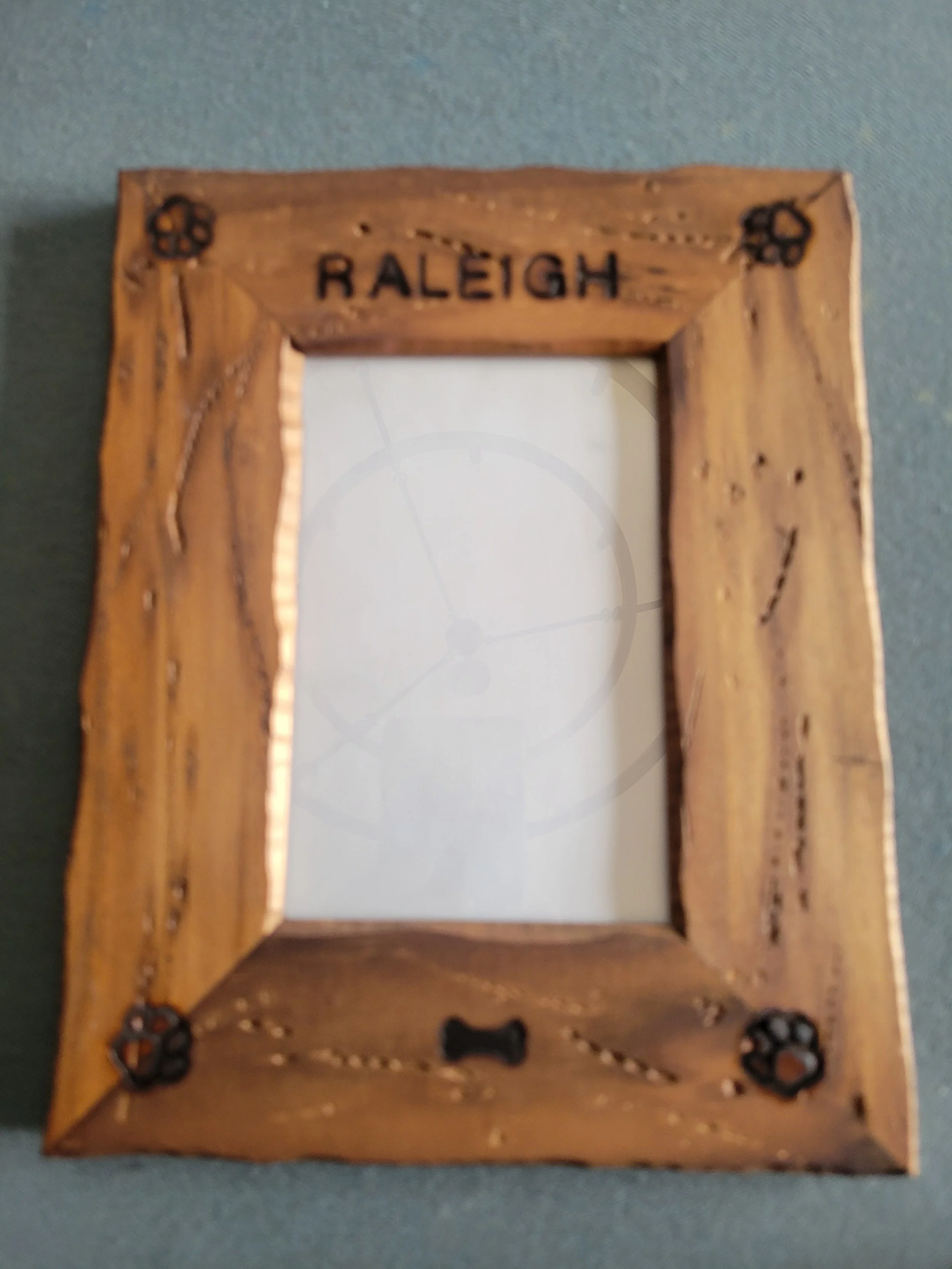 Wooden picture frame with the word 'Raleigh' engraved at the top, decorated with small paw prints in each corner.