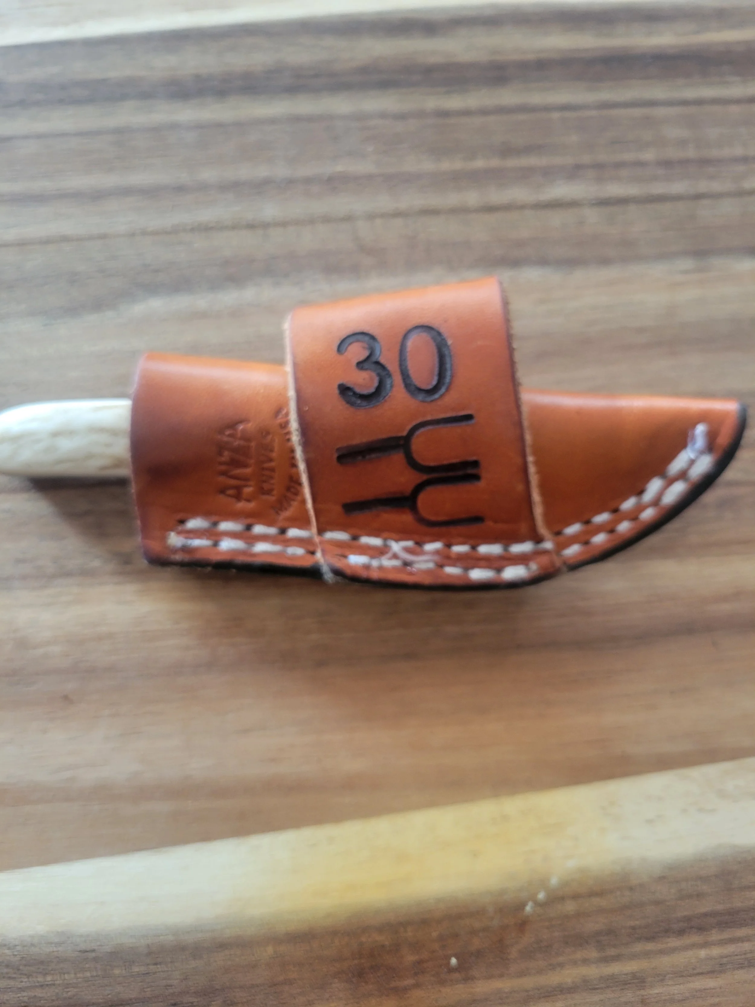 A small wooden paddle with a leather strap, painted with the number 30 and the word 'Yum' in black, placed on a wooden surface.