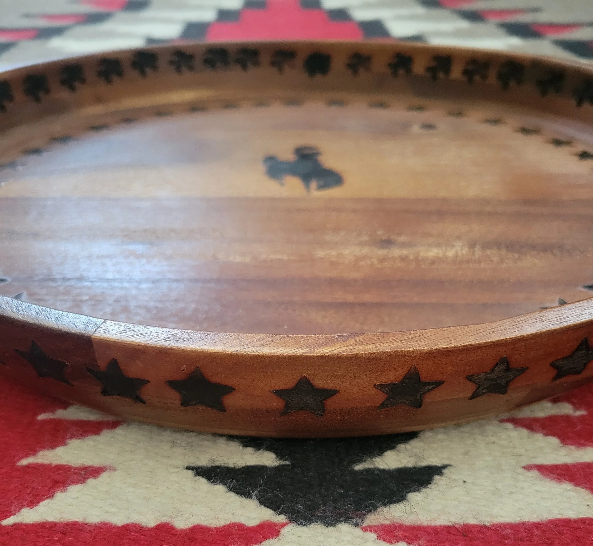 A round wooden tray with star-shaped cutouts around the rim, resting on a red, white, and black patterned surface.