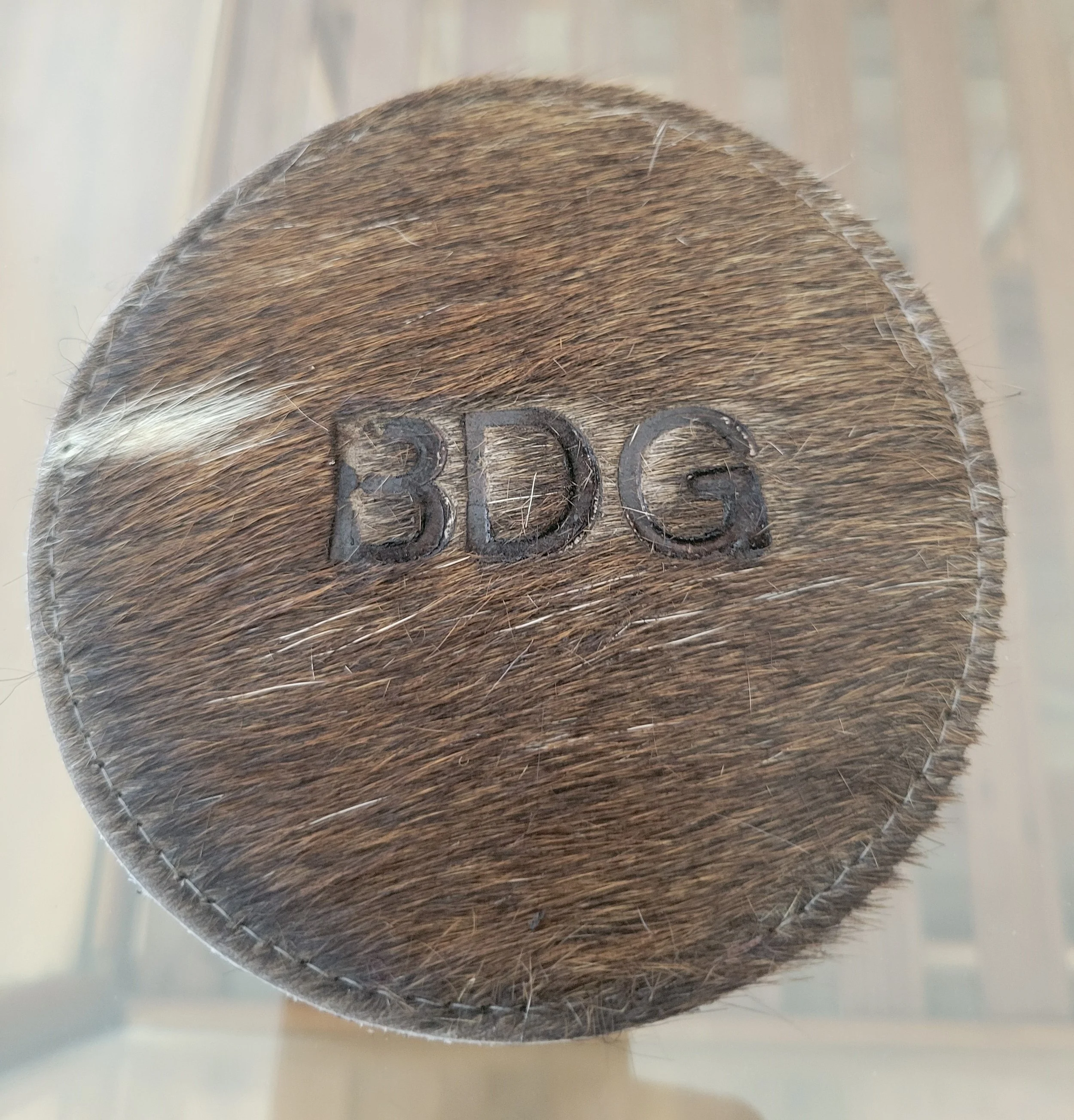 Close-up of a round wooden object with the engraved letters 'BDG' on its surface.