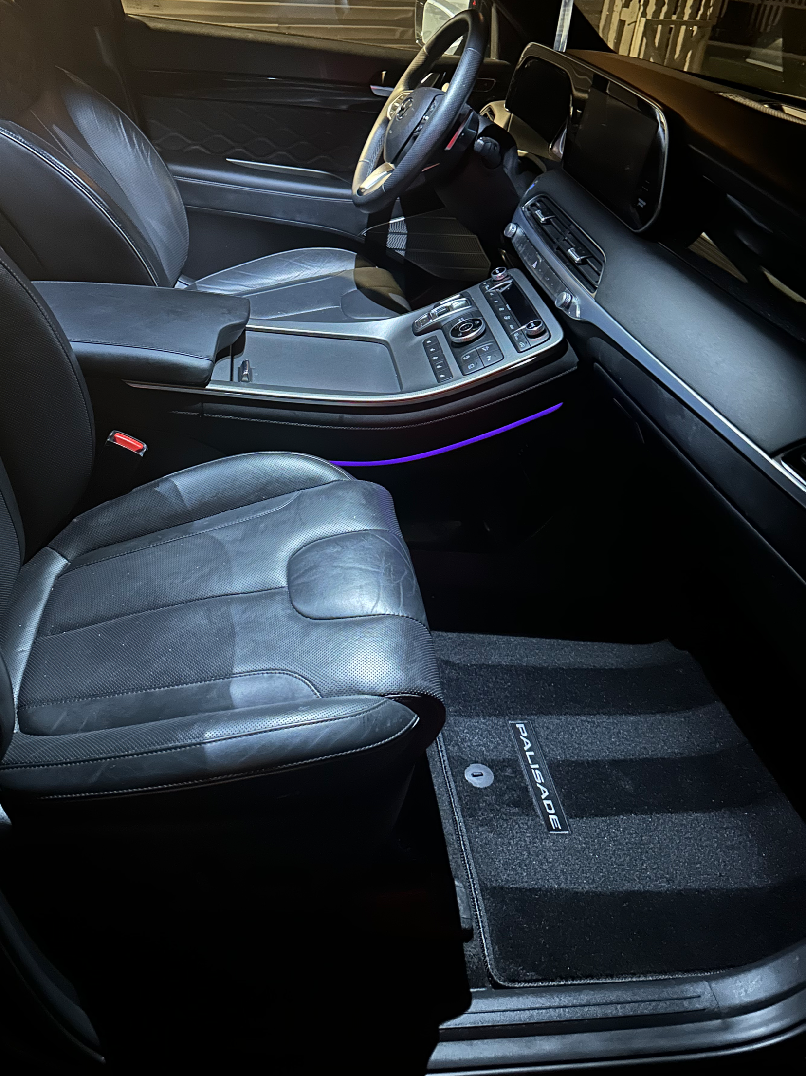 Interior of a vehicle showing the driver's seat and dashboard with a touchscreen display, gear shift, and floor mat with stripes.