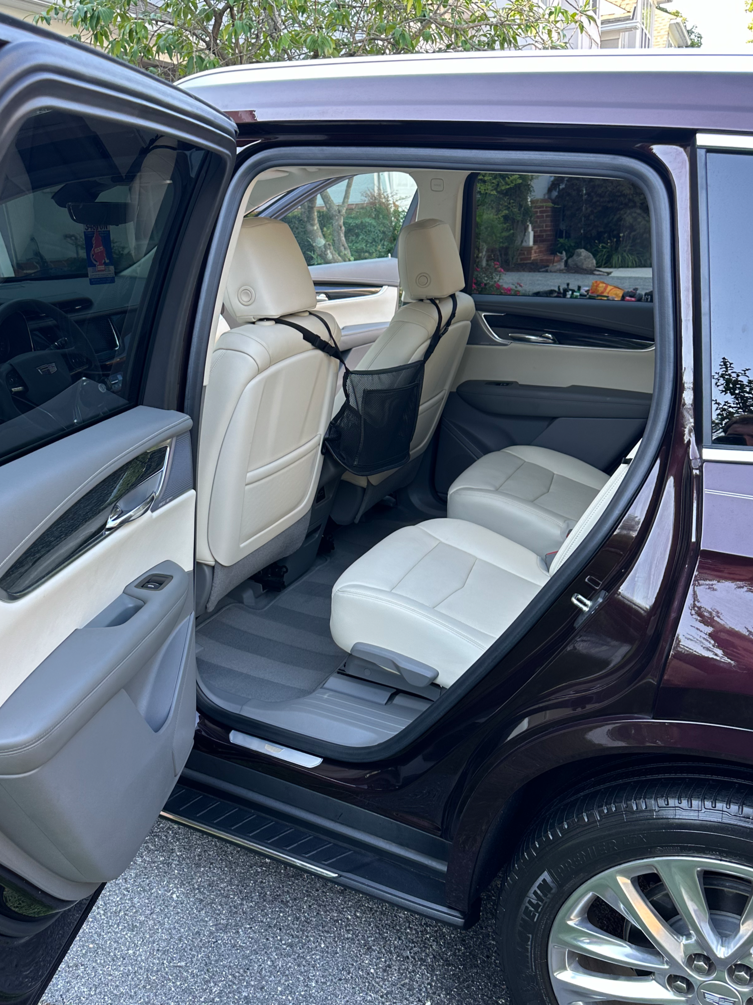 The interior of a black SUV with white leather seats, showing the open rear door, front seats, backseat, and a storage pocket behind the front passenger seat.