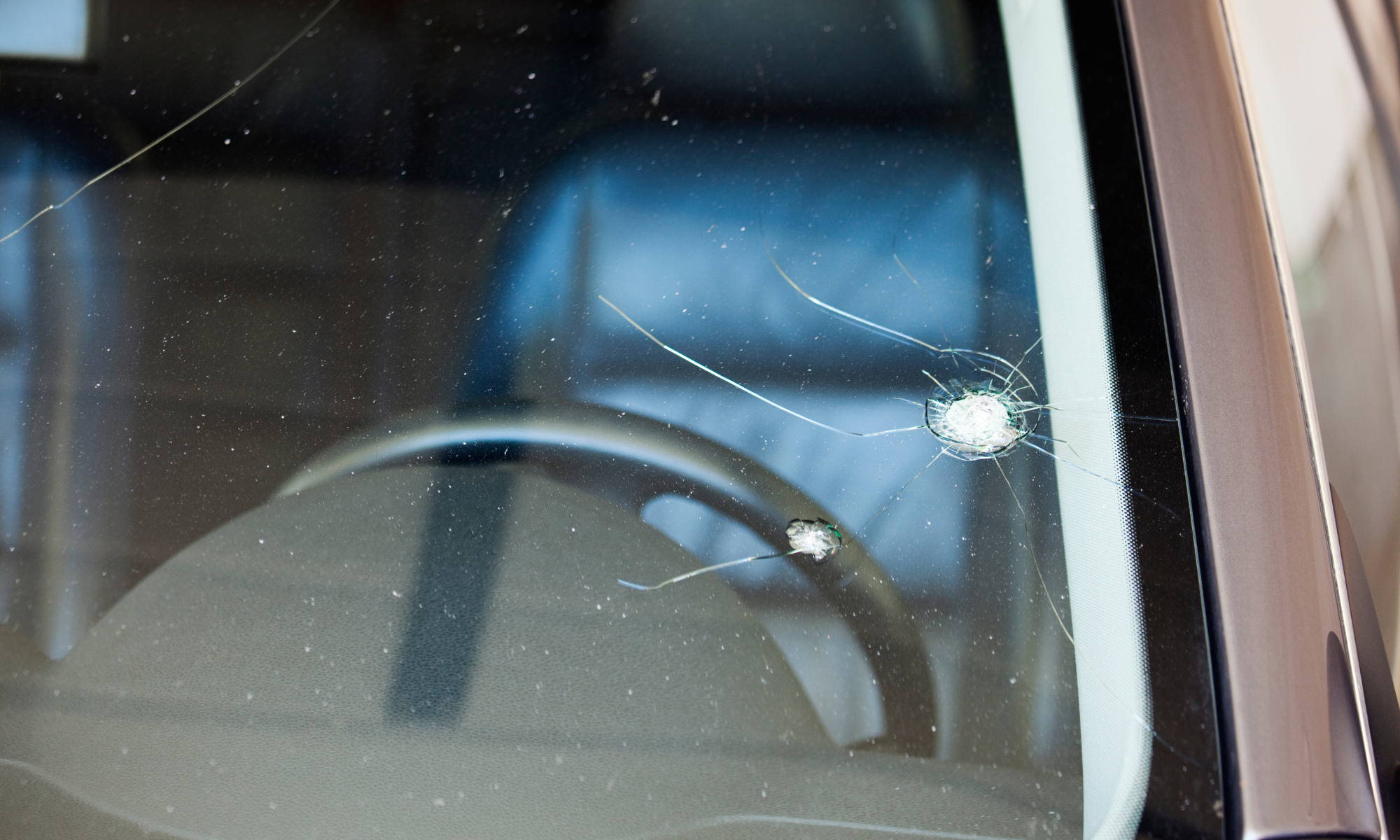 Close-up of a car windshield with two large cracks and shattered glass.