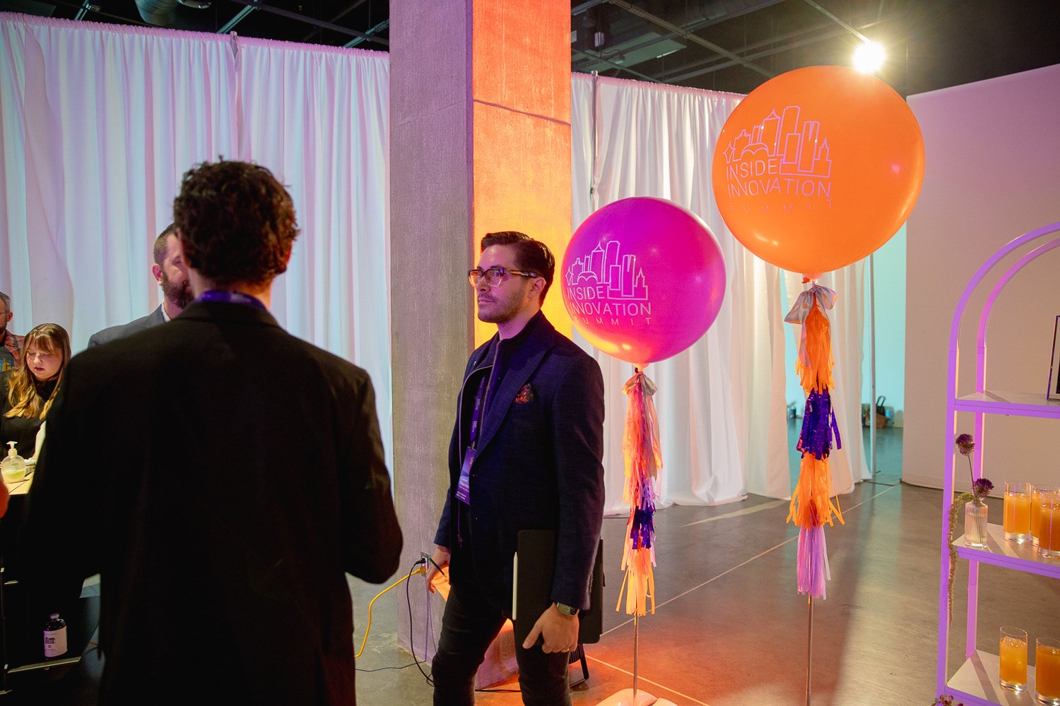 People talking at a business event called Inside Innovation Summit with pink and orange balloons in the background.