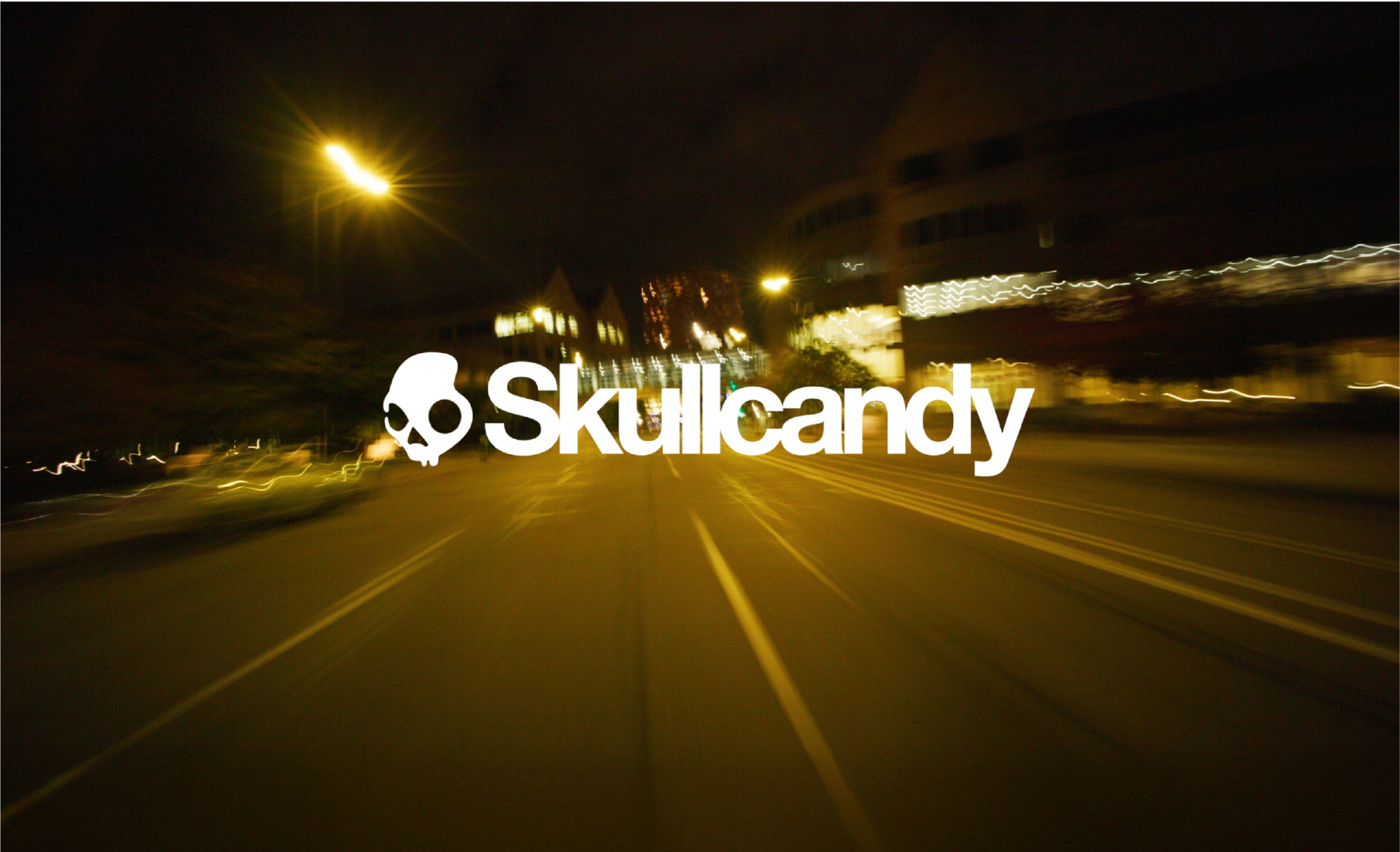 Nighttime city street with blurred lights and a prominent white skull logo and text reading "skullcandy" in the center.